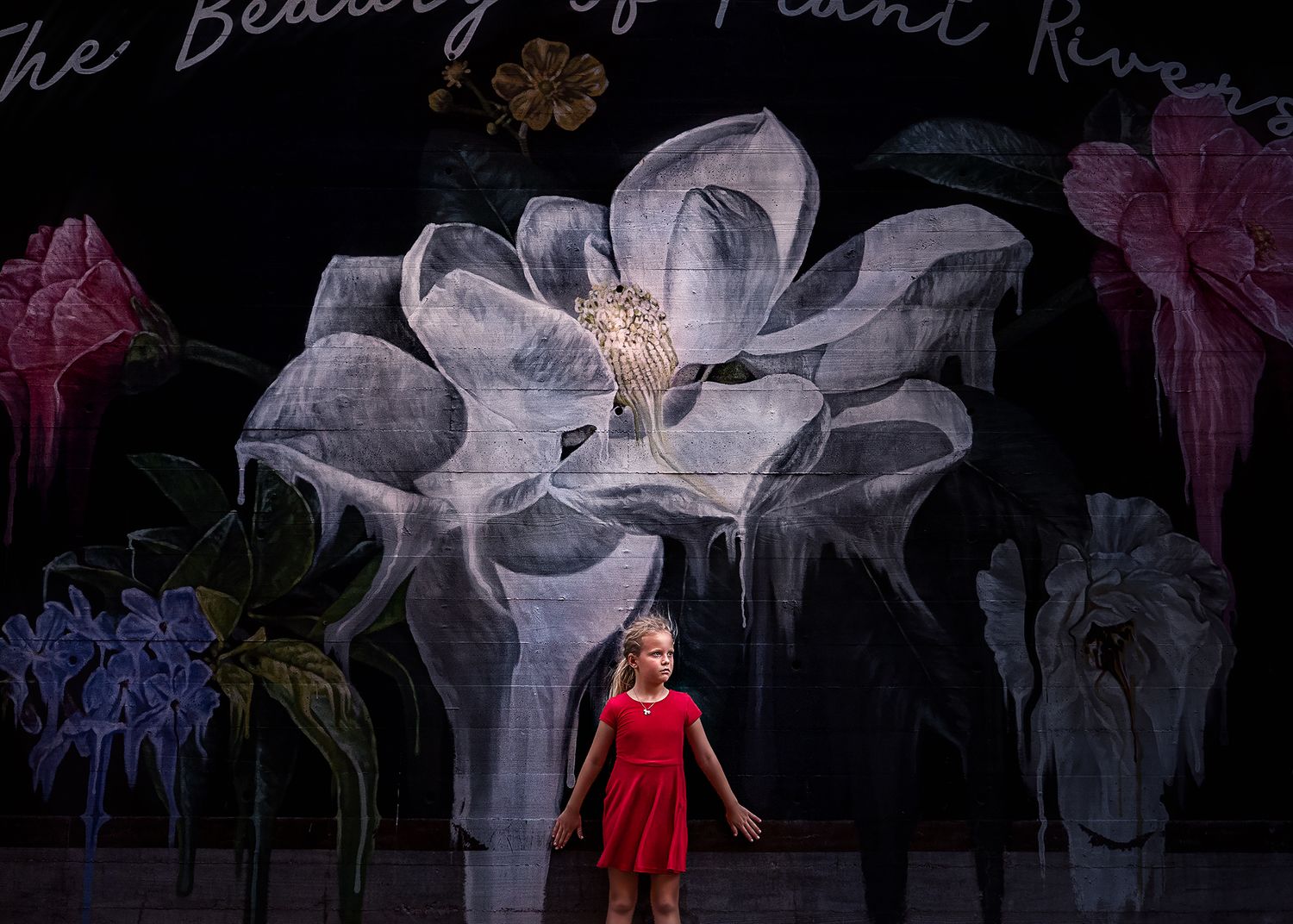 A young girl in a red dress performs on stage in front of a large floral backdrop with painted flowers.