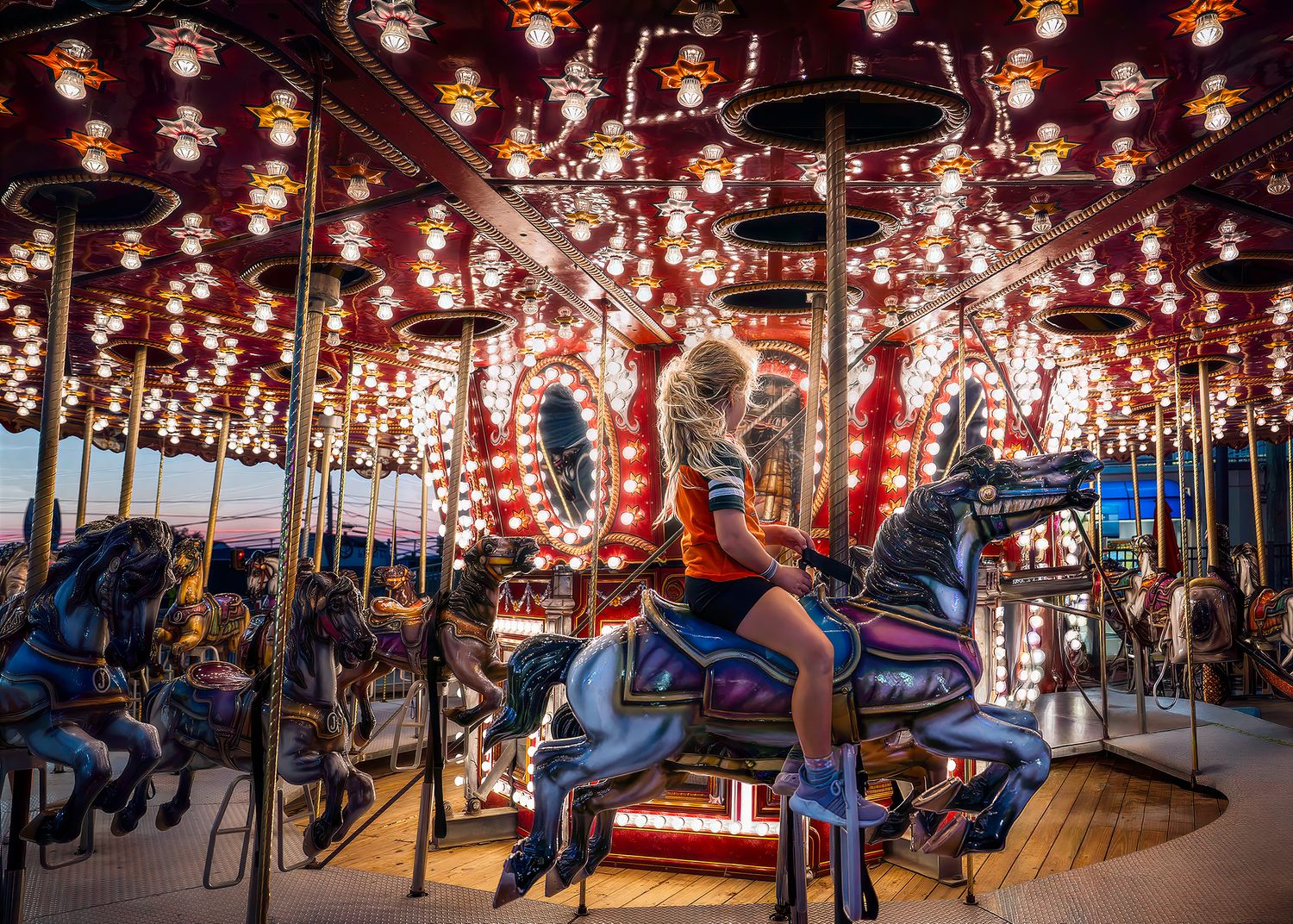 A woman rides a decorated carousel horse on a brightly lit merry-go-round at a festive fairground.