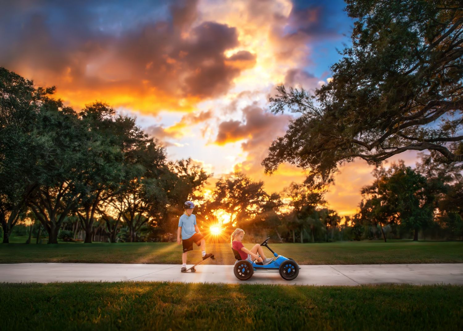 Two children play with a pedal go-kart on a path during a stunning colorful sunset.