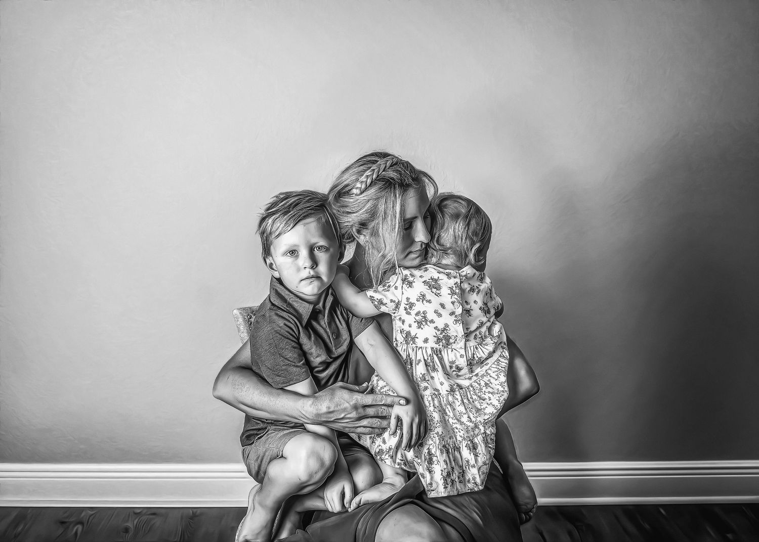 Black and white photo of a mother sitting on the floor holding two young children tenderly.