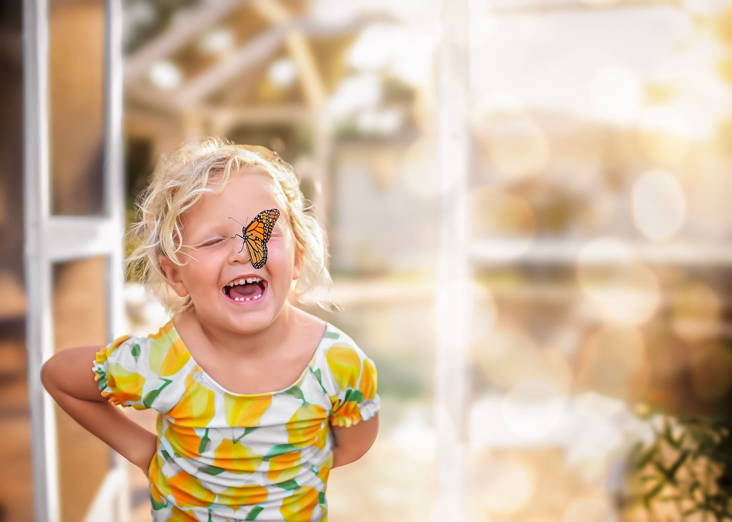 Joyful blonde girl laughing with a monarch butterfly perched on her cheek.