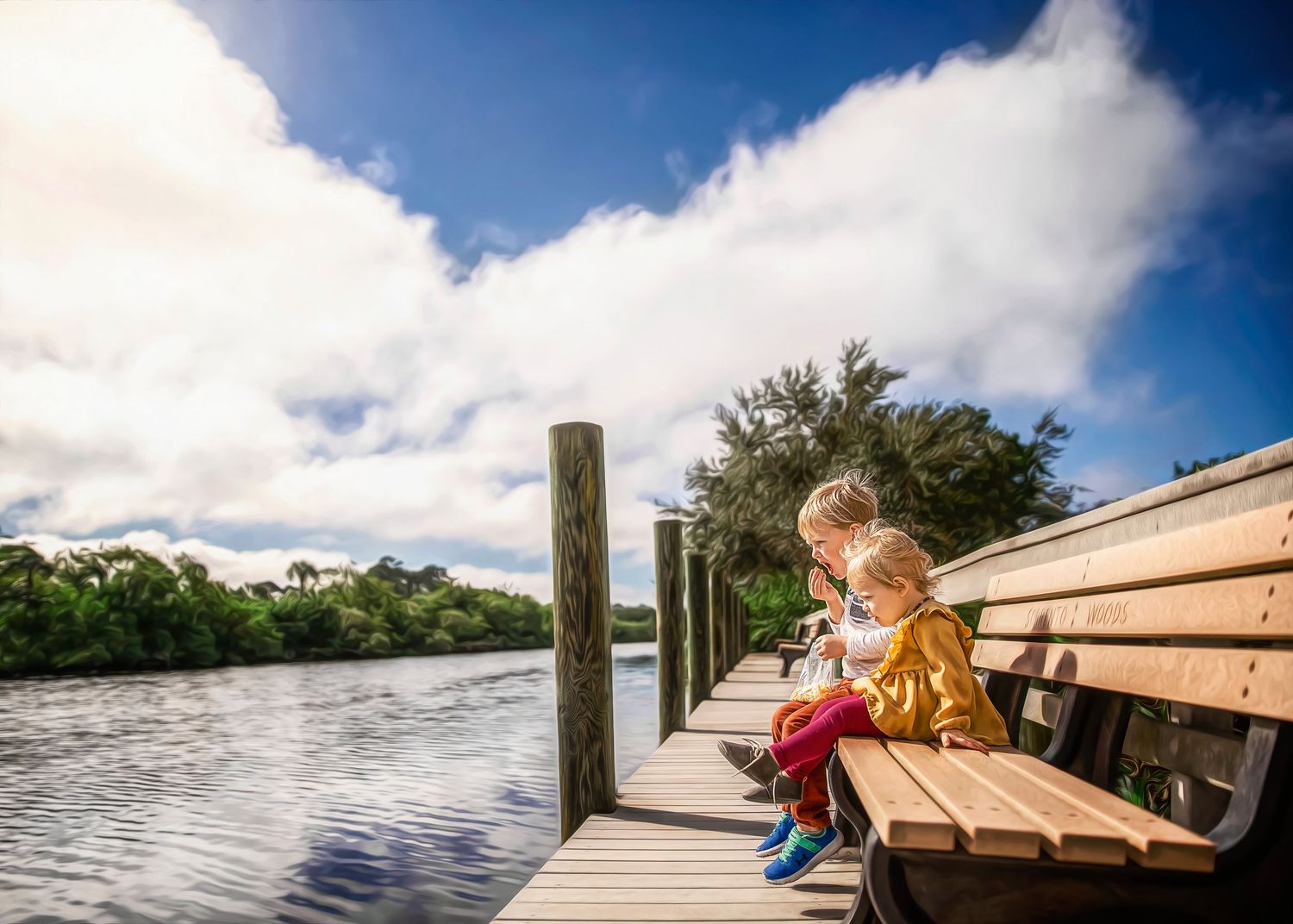 Two young children sitting on a wooden dock bench overlooking a scenic river.