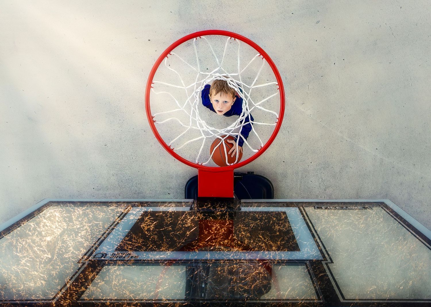 Overhead view of a boy holding a basketball seen through a basketball hoop and net.