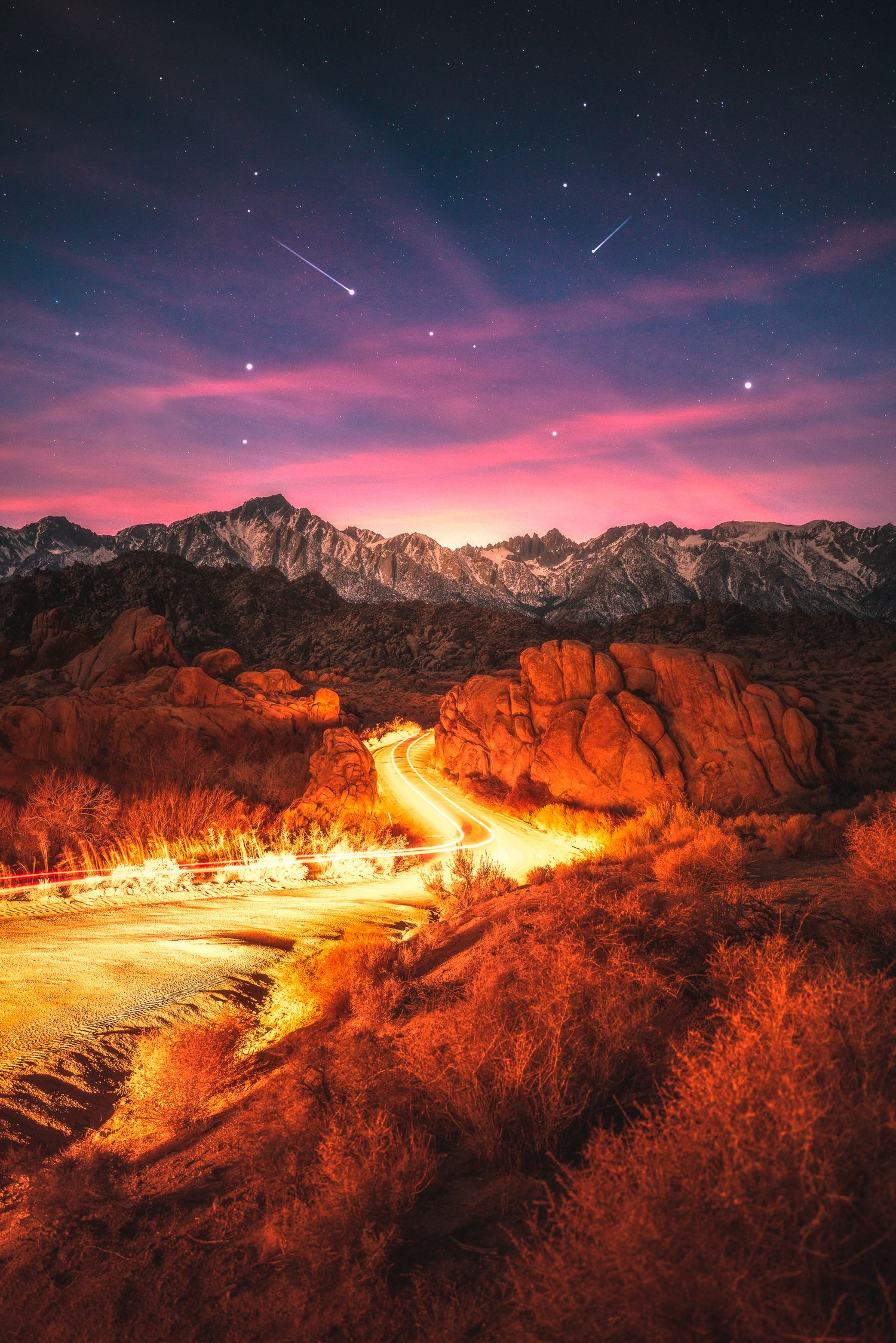 Light trails wind through Alabama Hills at night with shooting stars over Sierra Nevada mountains.