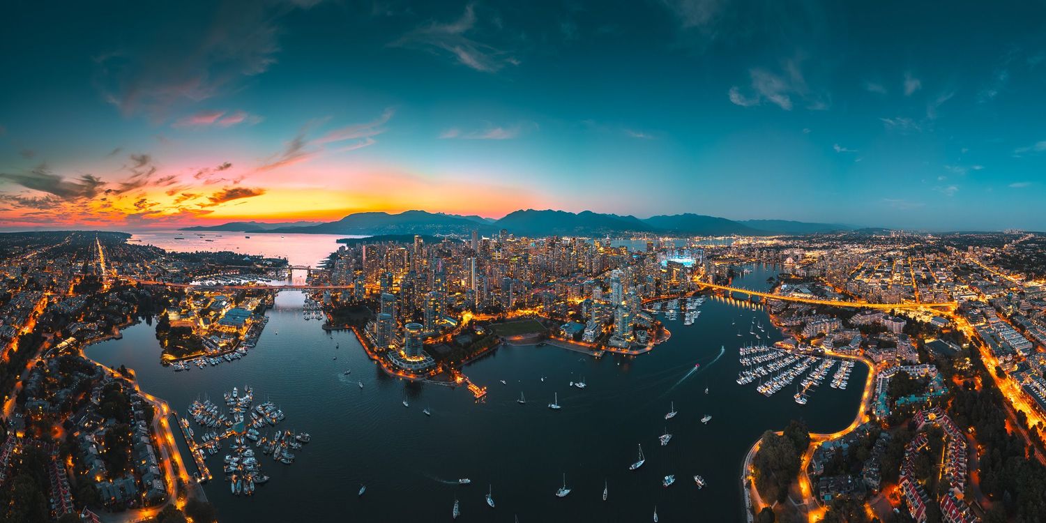 Stunning panoramic aerial sunset view of Vancouver's downtown skyline surrounded by sparkling harbor waters and mountains.