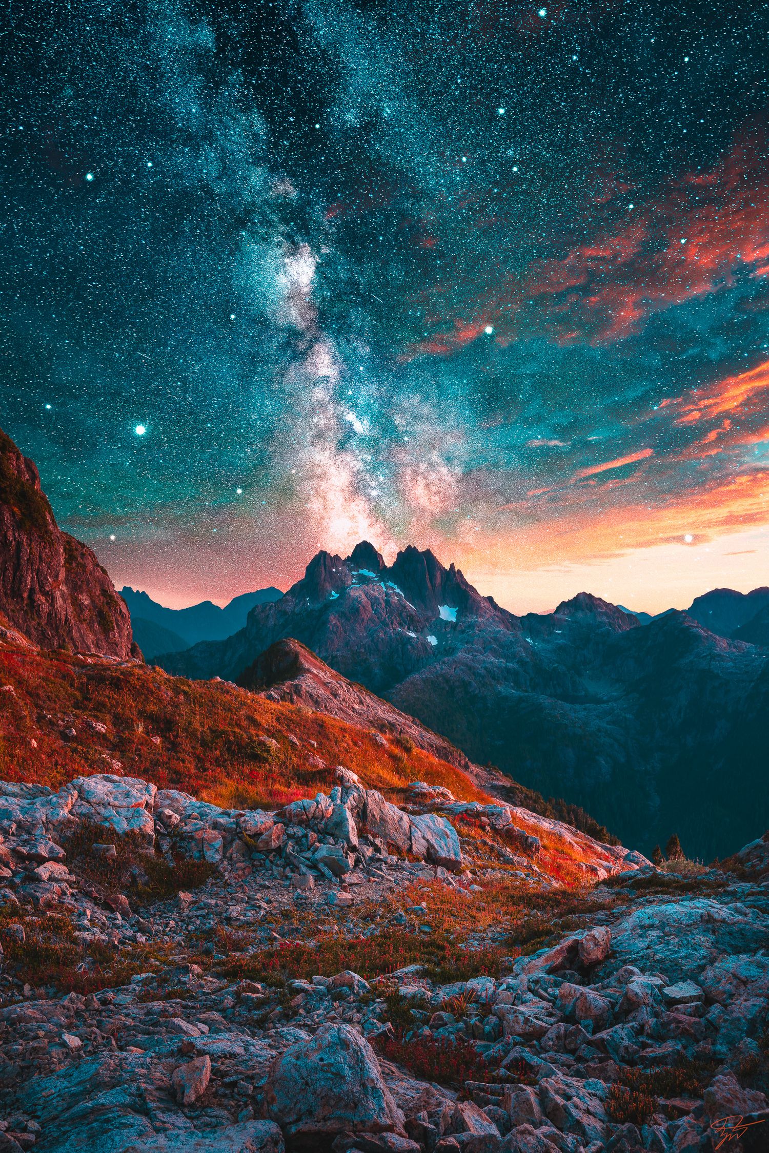 Vibrant Milky Way and colorful clouds illuminate a dramatic mountain range with rocky terrain at twilight.