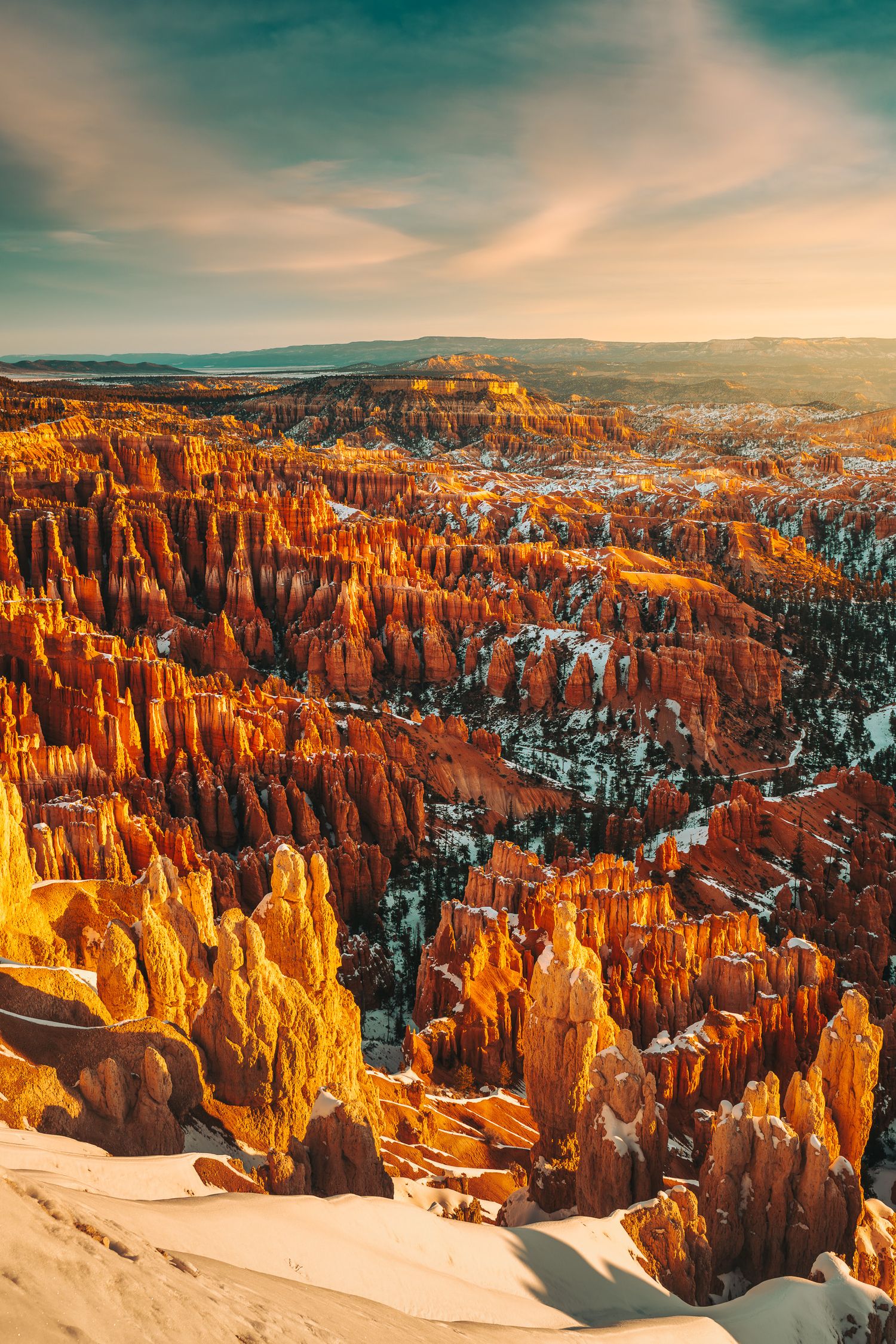 Aerial view of Bryce Canyon hoodoos glowing orange at sunrise with light snow dusting, Utah, USA.