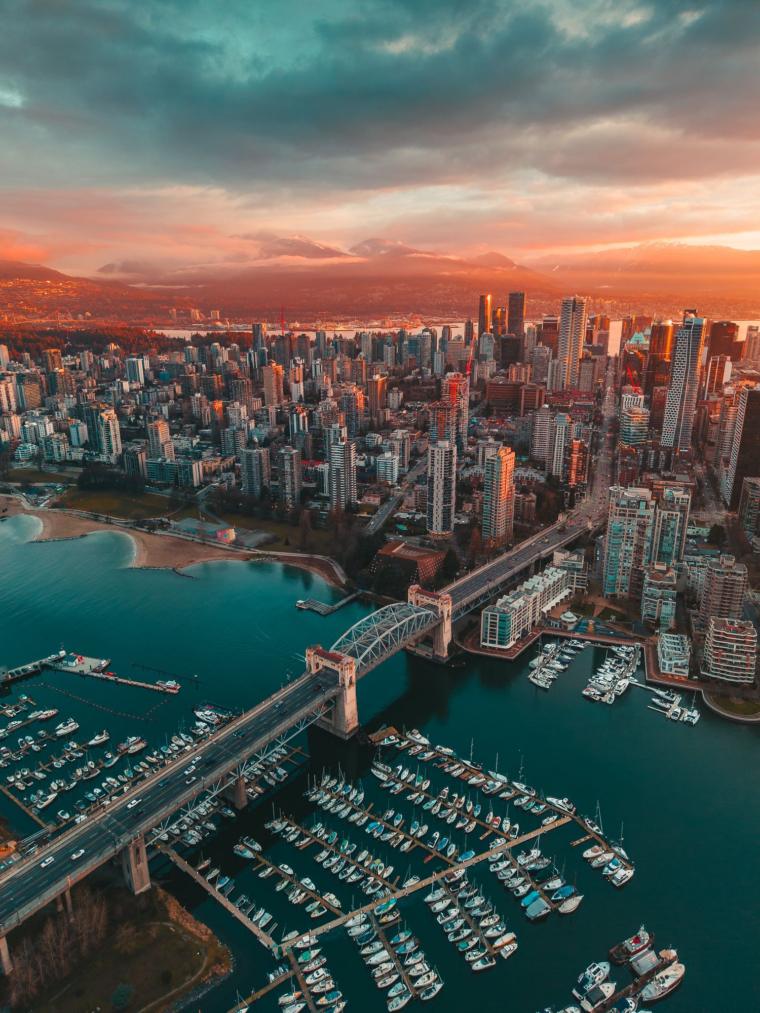 Aerial sunset panorama of Vancouver with Burrard Bridge, marina, and golden-lit city skyline.