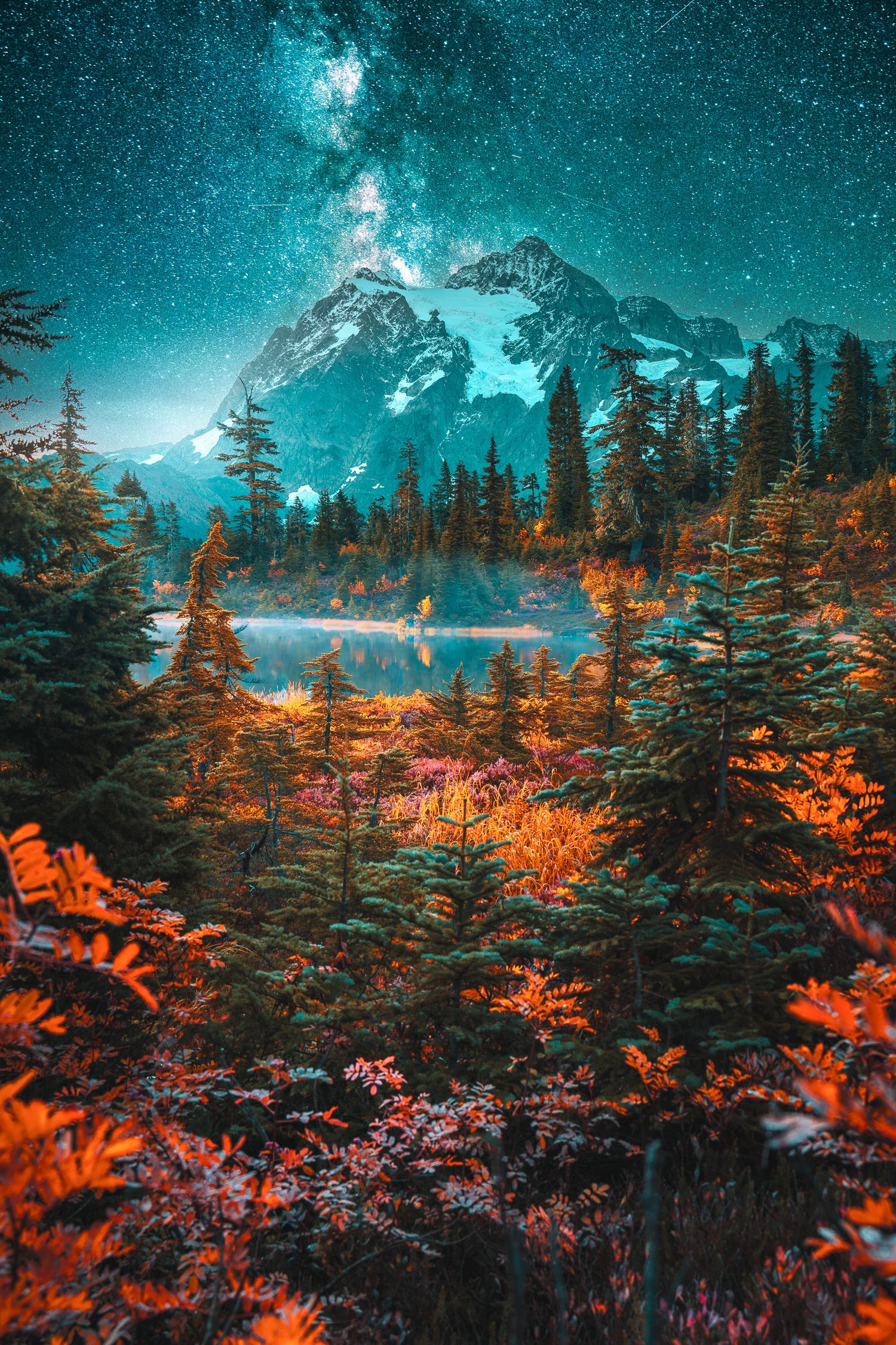 Milky Way shines over a snow-capped mountain reflected in a serene alpine lake surrounded by colorful autumn forest.
