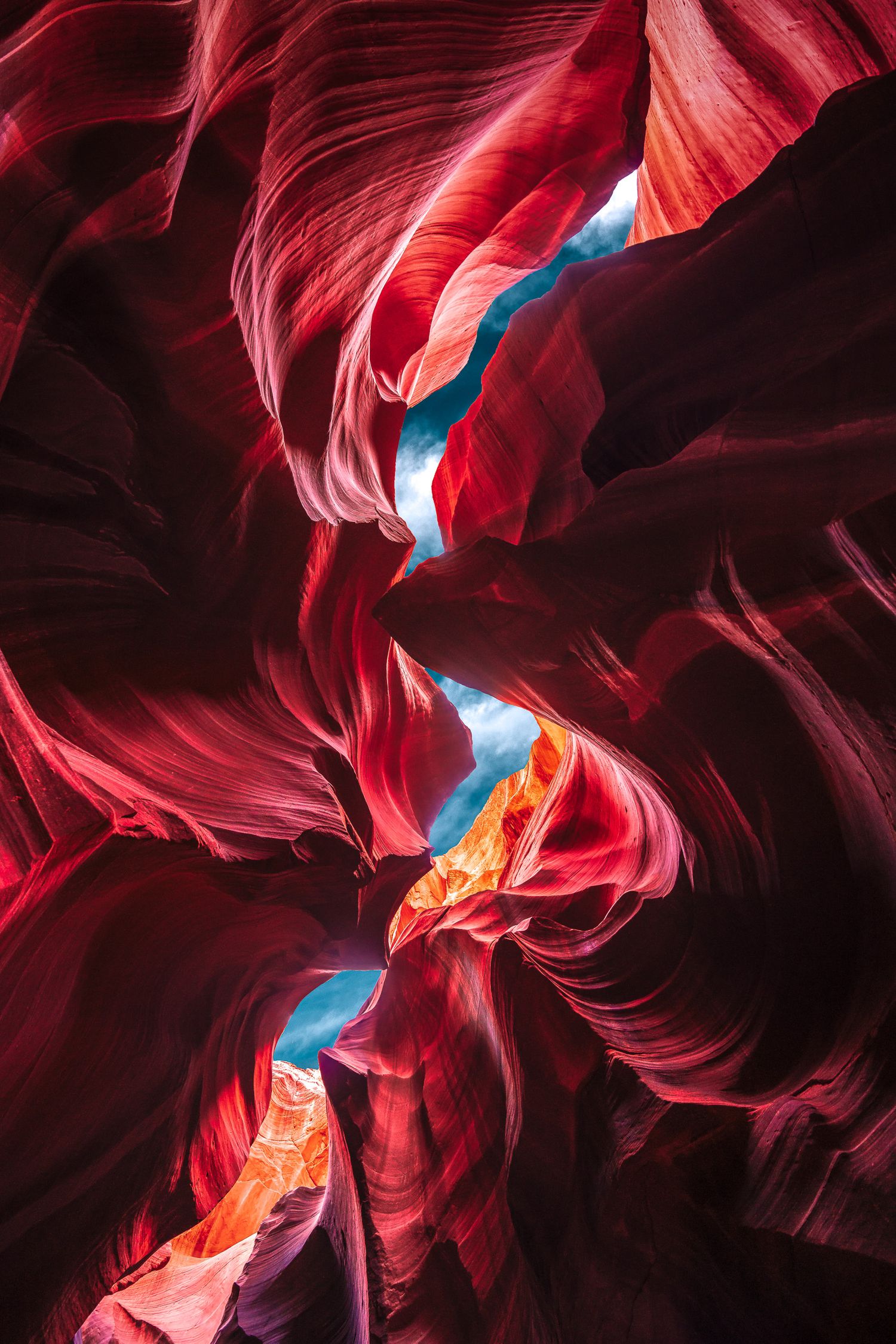 Stunning red and orange sandstone waves inside Antelope Canyon with blue sky peeking through the narrow slot.