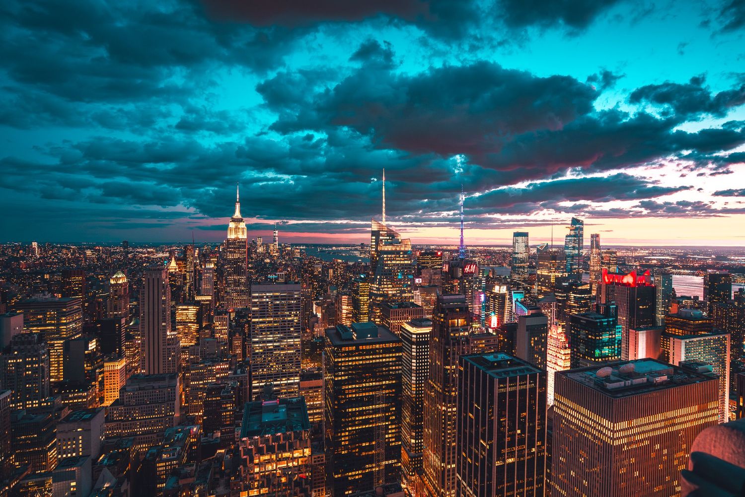 New York City skyline at twilight with Empire State Building glowing under teal storm clouds.