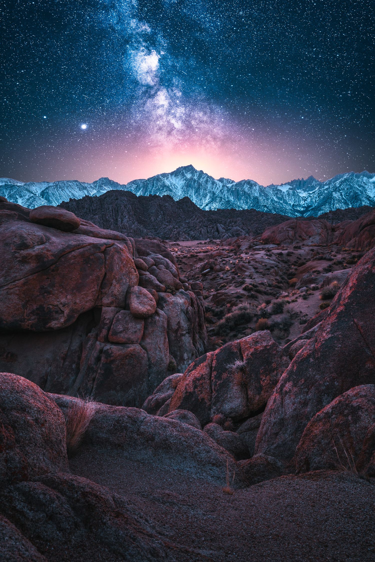Milky Way galaxy over snow-capped Sierra Nevada mountains with rugged Alabama Hills rock formations at night.