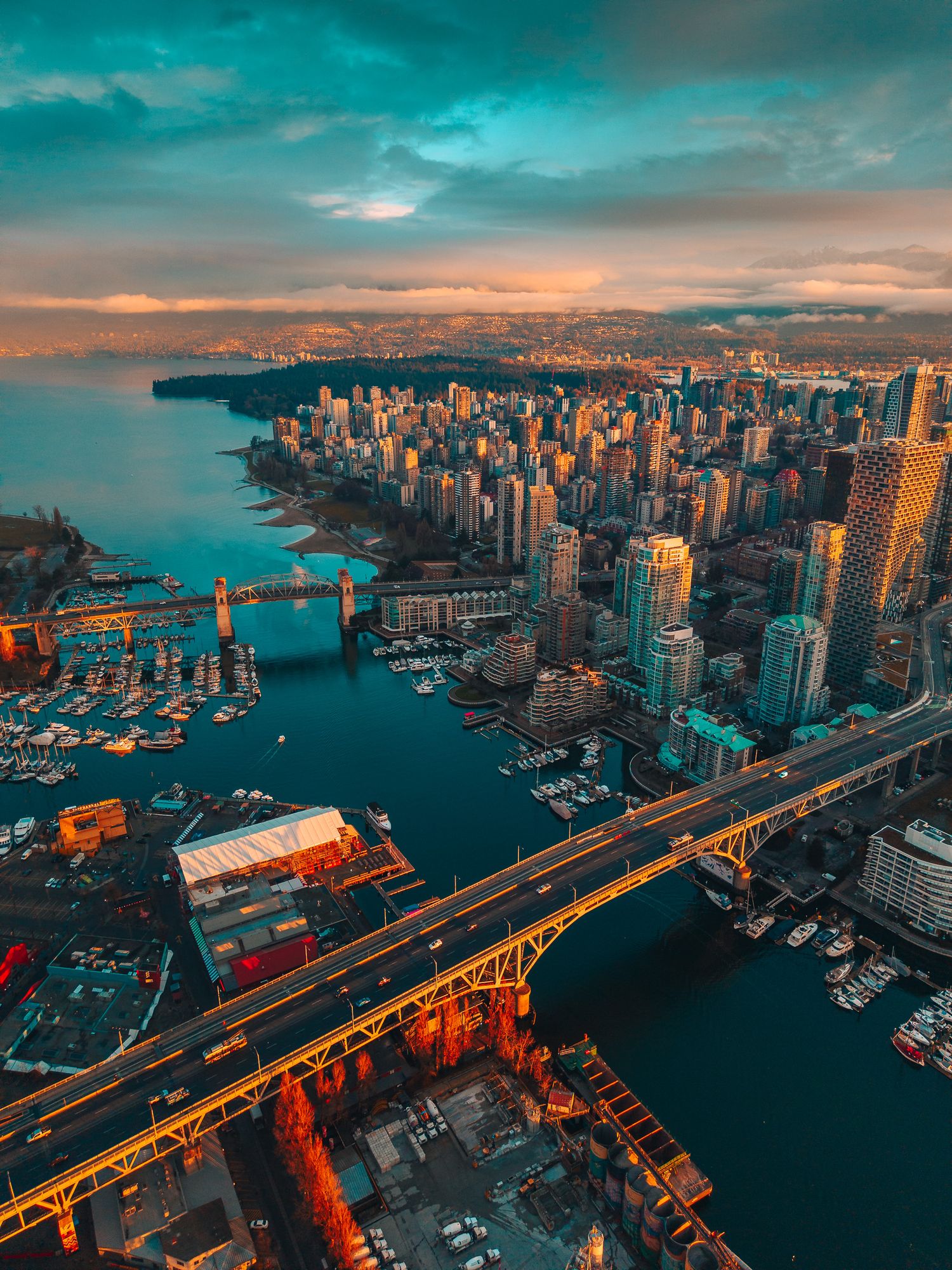 Aerial view of Vancouver skyline at sunset with bridges, harbor, and dramatic teal and orange sky.
