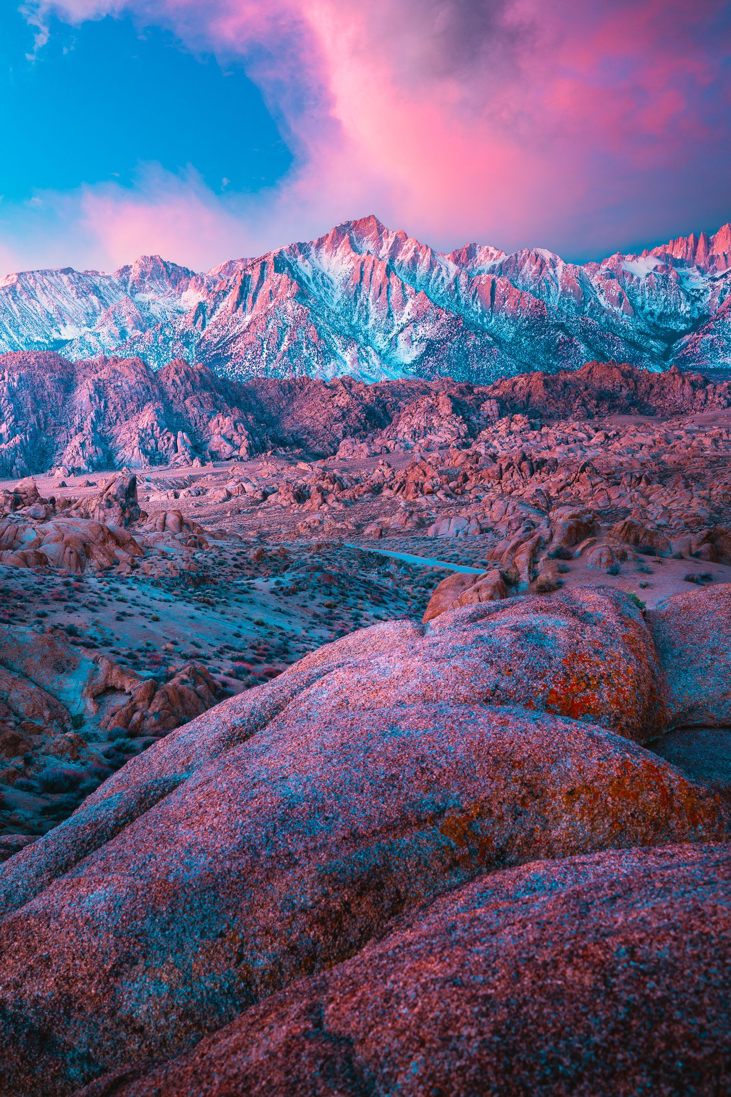 Dramatic pink sunset sky over rugged Alabama Hills boulders with snow-capped Sierra Nevada mountains.
