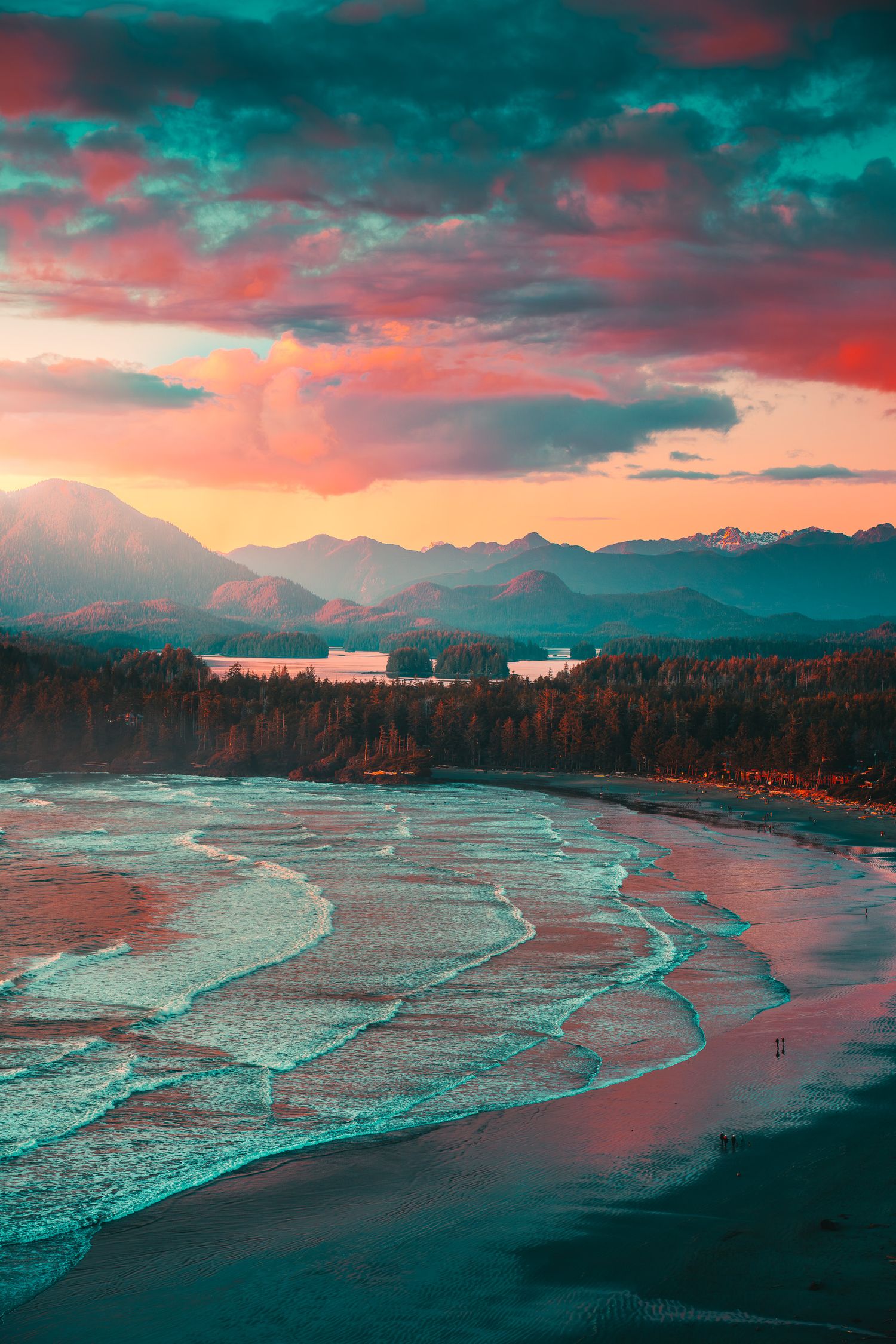 Aerial view of a stunning coastal sunset with turquoise waves, dense forest, and mountain range under a vivid pink sky.