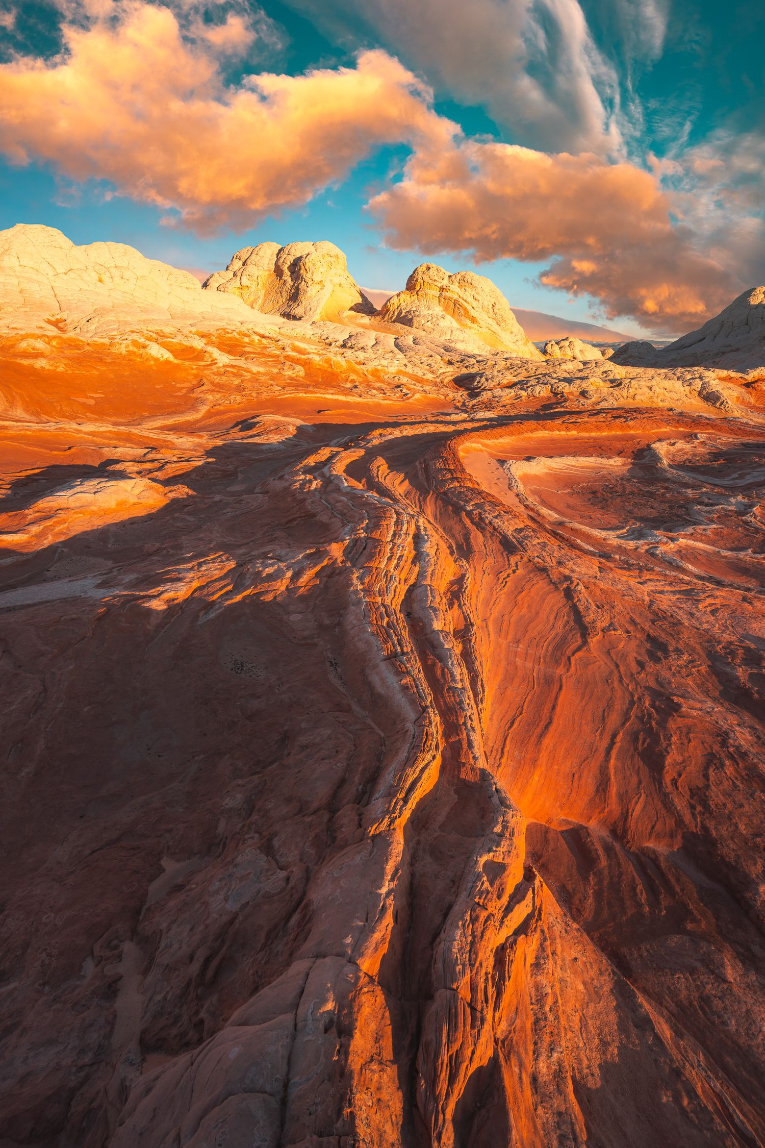 Dramatic orange and white sandstone rock formations with sweeping curves glowing under a vibrant sunset sky.