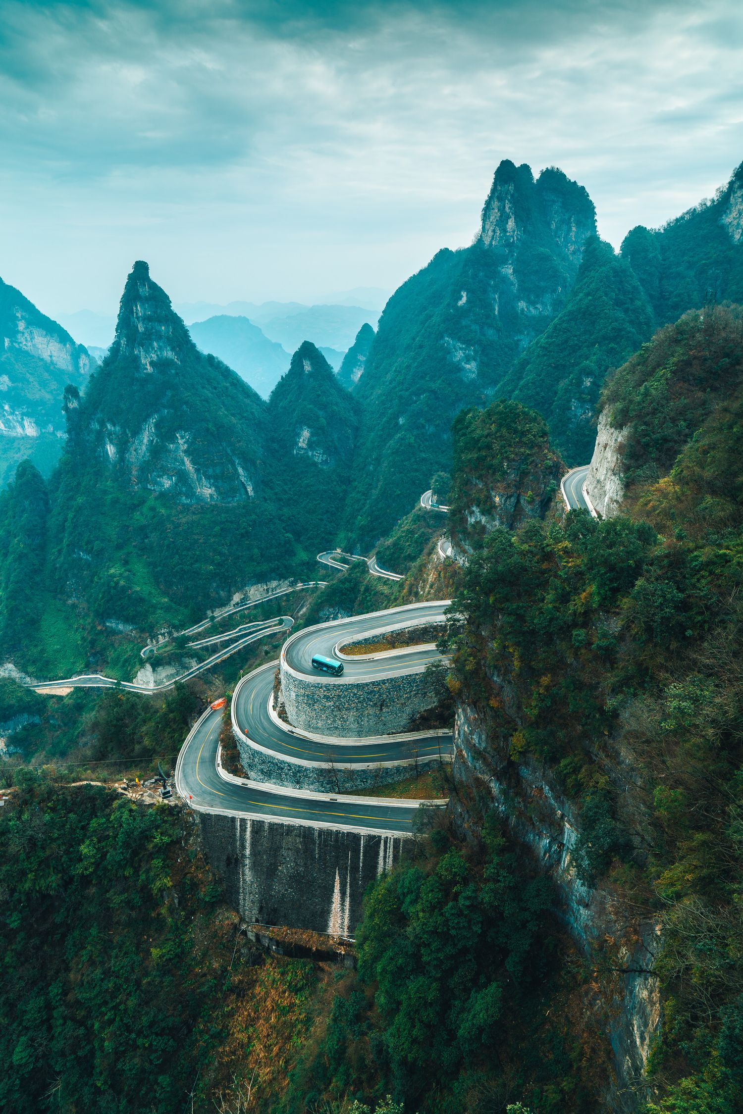Aerial view of a dramatic winding mountain road with sharp switchbacks through lush green karst peaks.