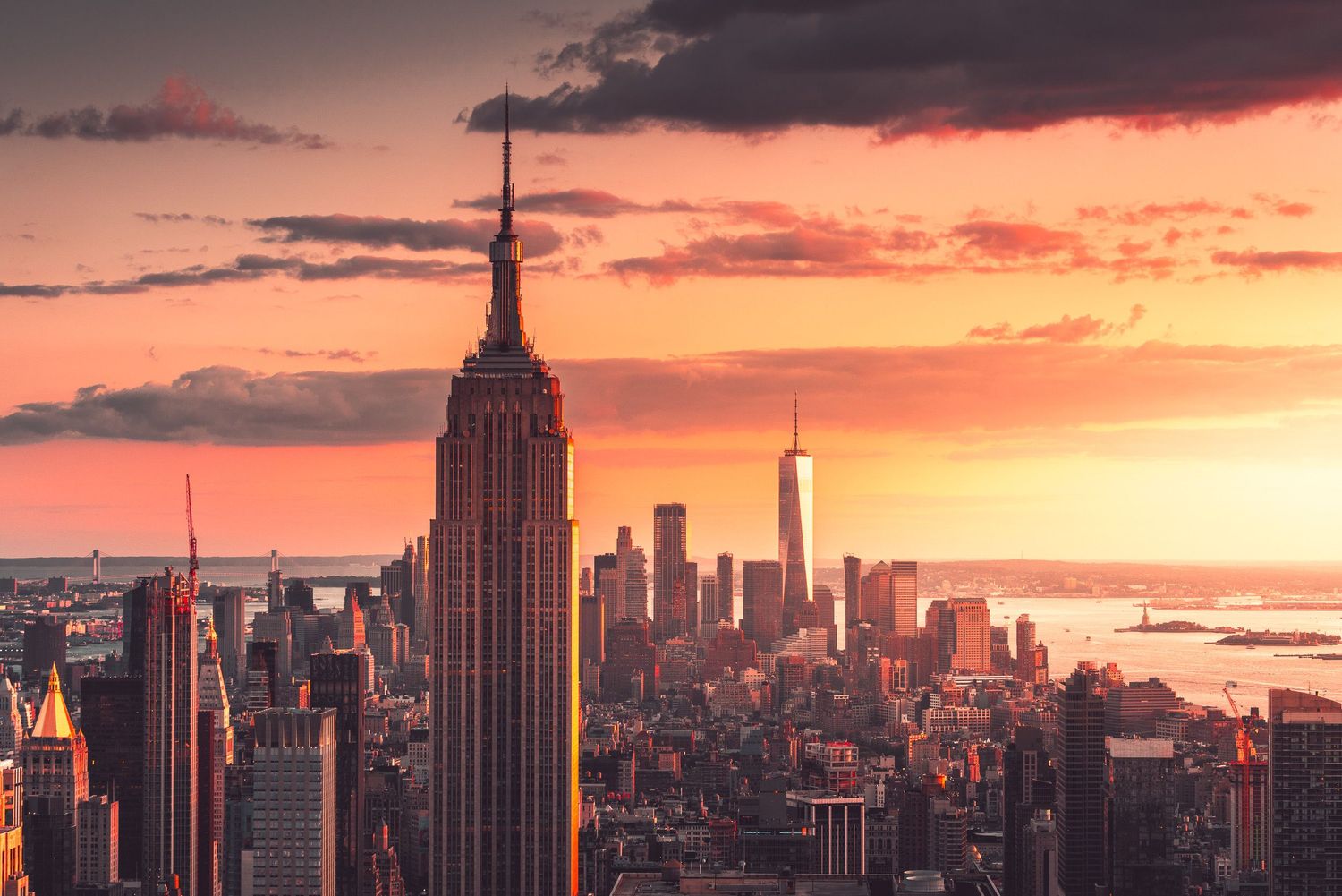 Aerial view of Manhattan at sunset with Empire State Building and teal-toned dramatic cloudscape.