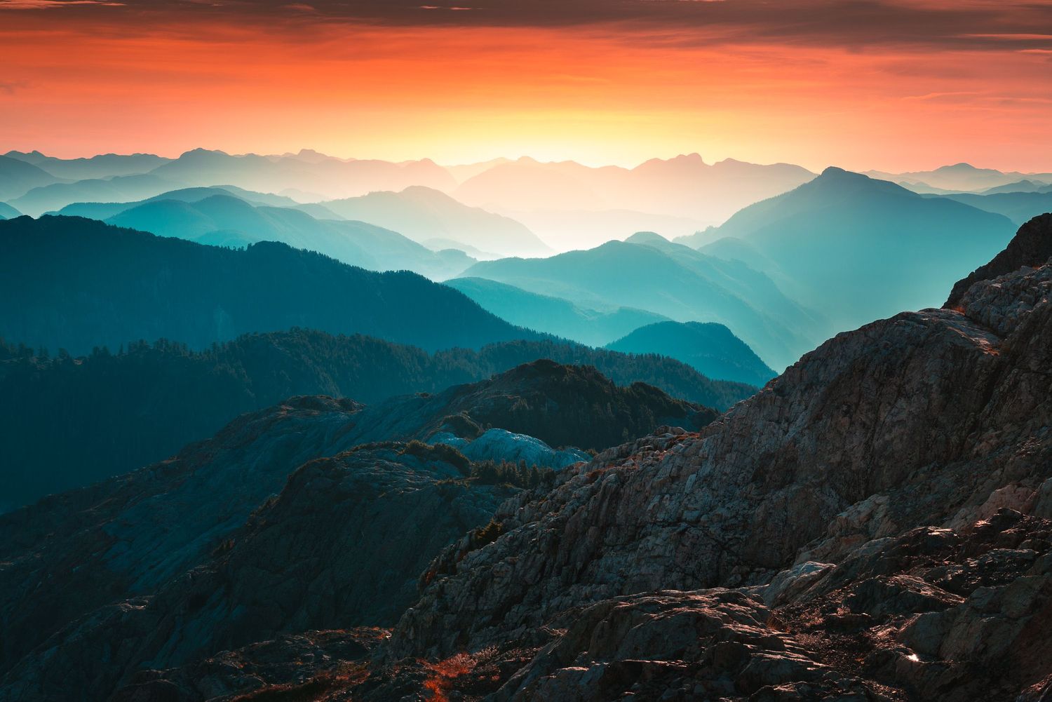 Stunning mountain range sunset with vibrant orange sky and layered blue ridges fading into the horizon.