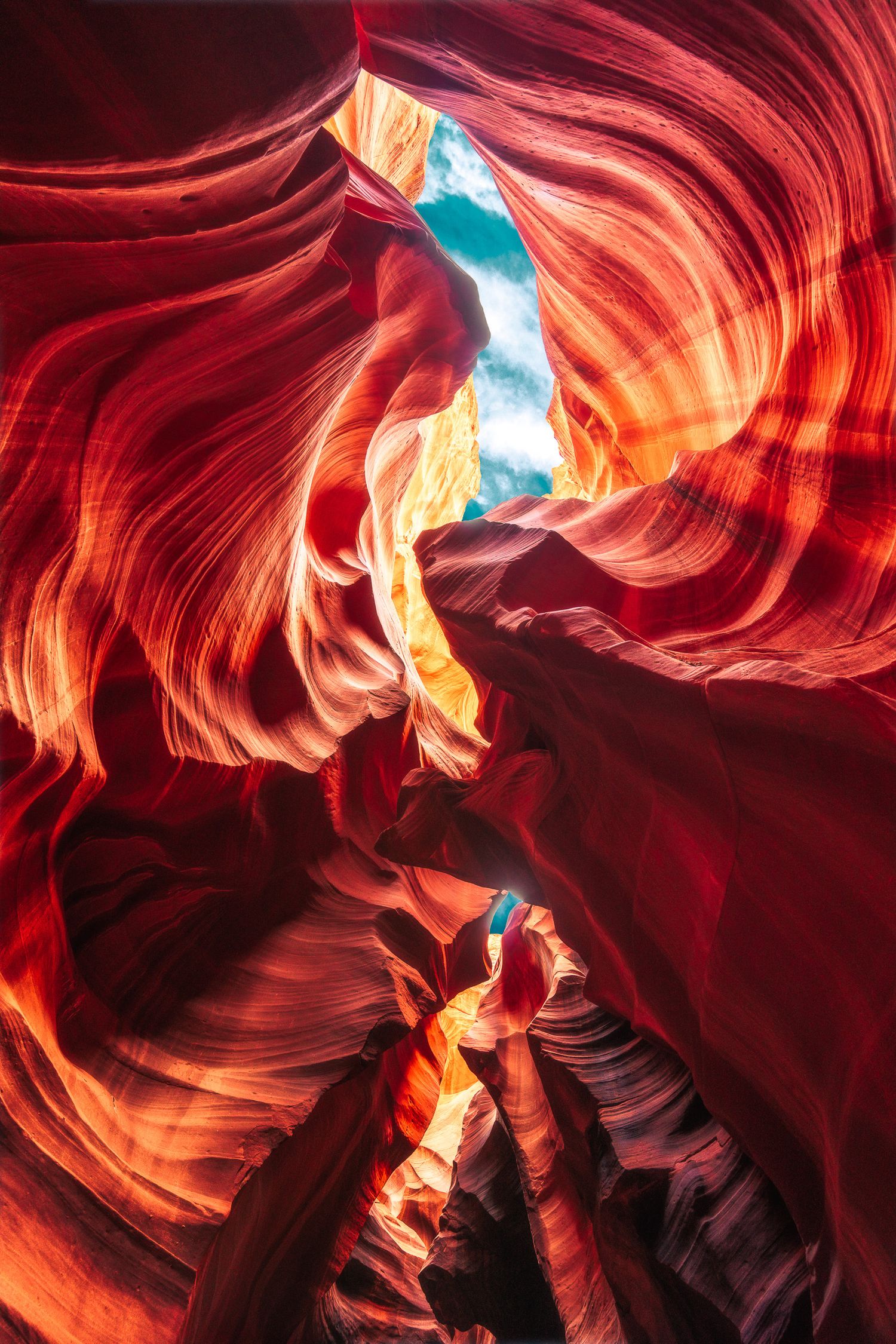 Breathtaking red and orange sandstone walls of Antelope Canyon with a narrow opening revealing blue sky.