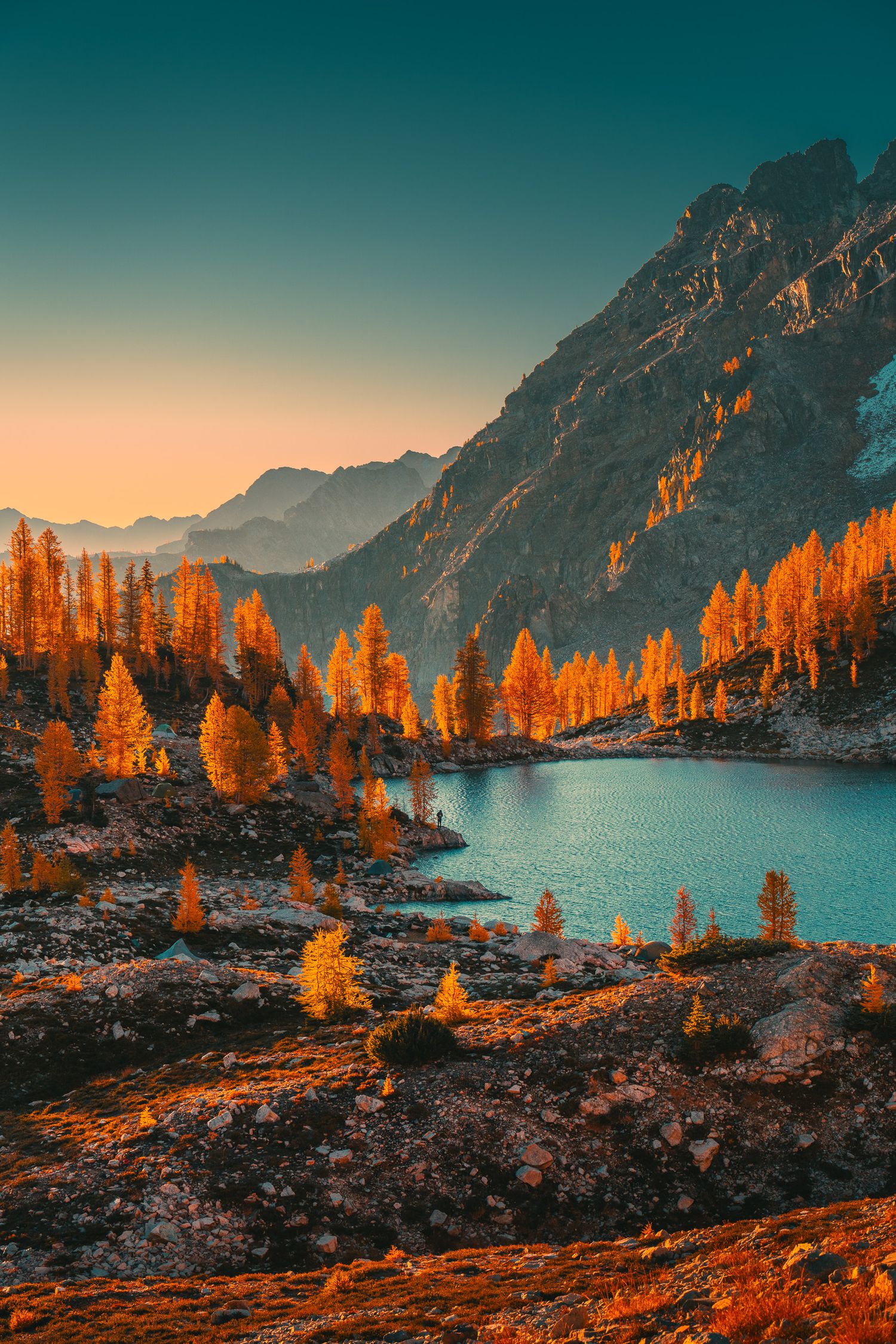 Autumn alpine lake surrounded by golden larch trees and rocky mountains at sunset.