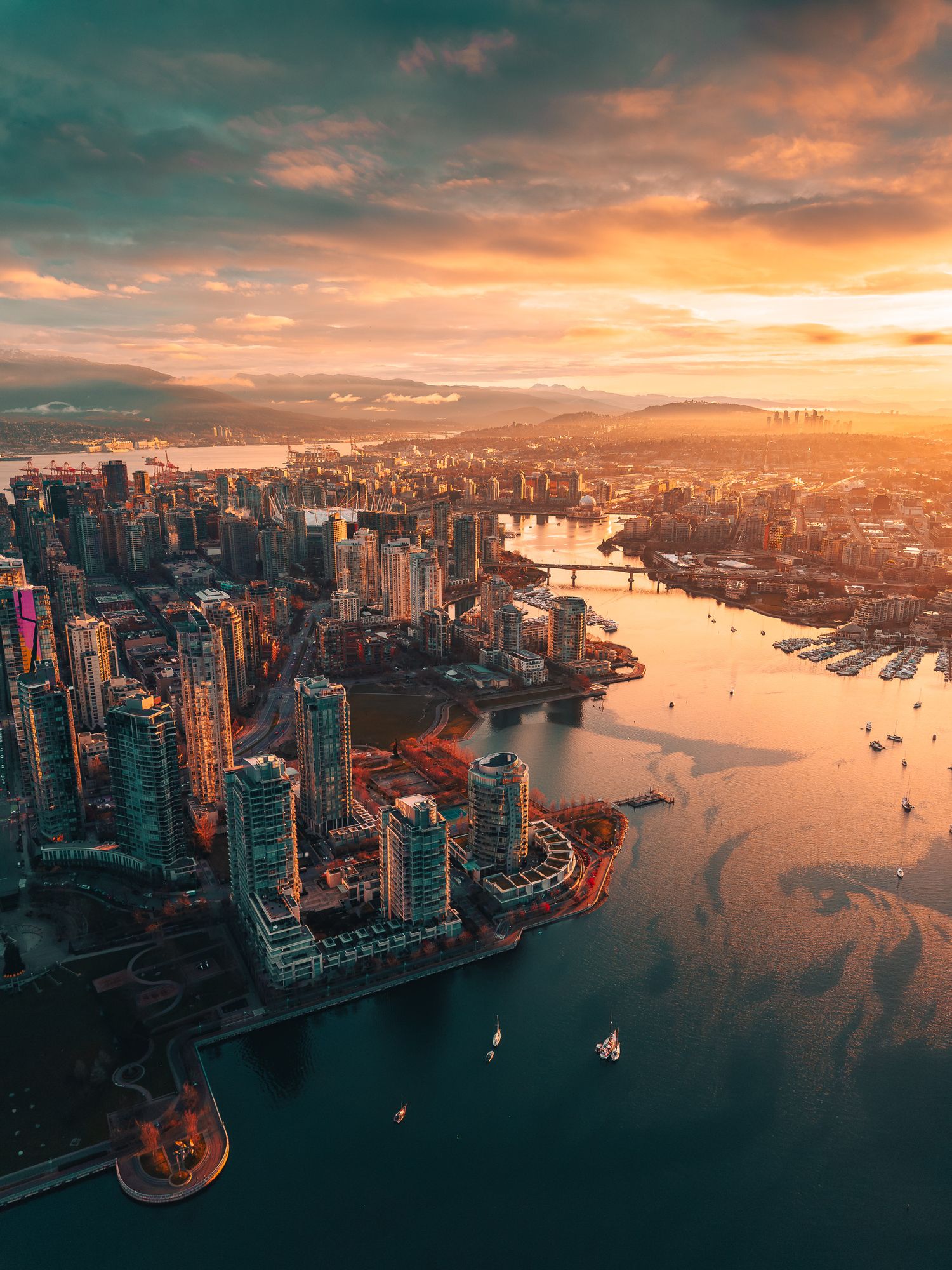 Golden sunset aerial view of Vancouver skyline reflecting warm light over False Creek waterway.