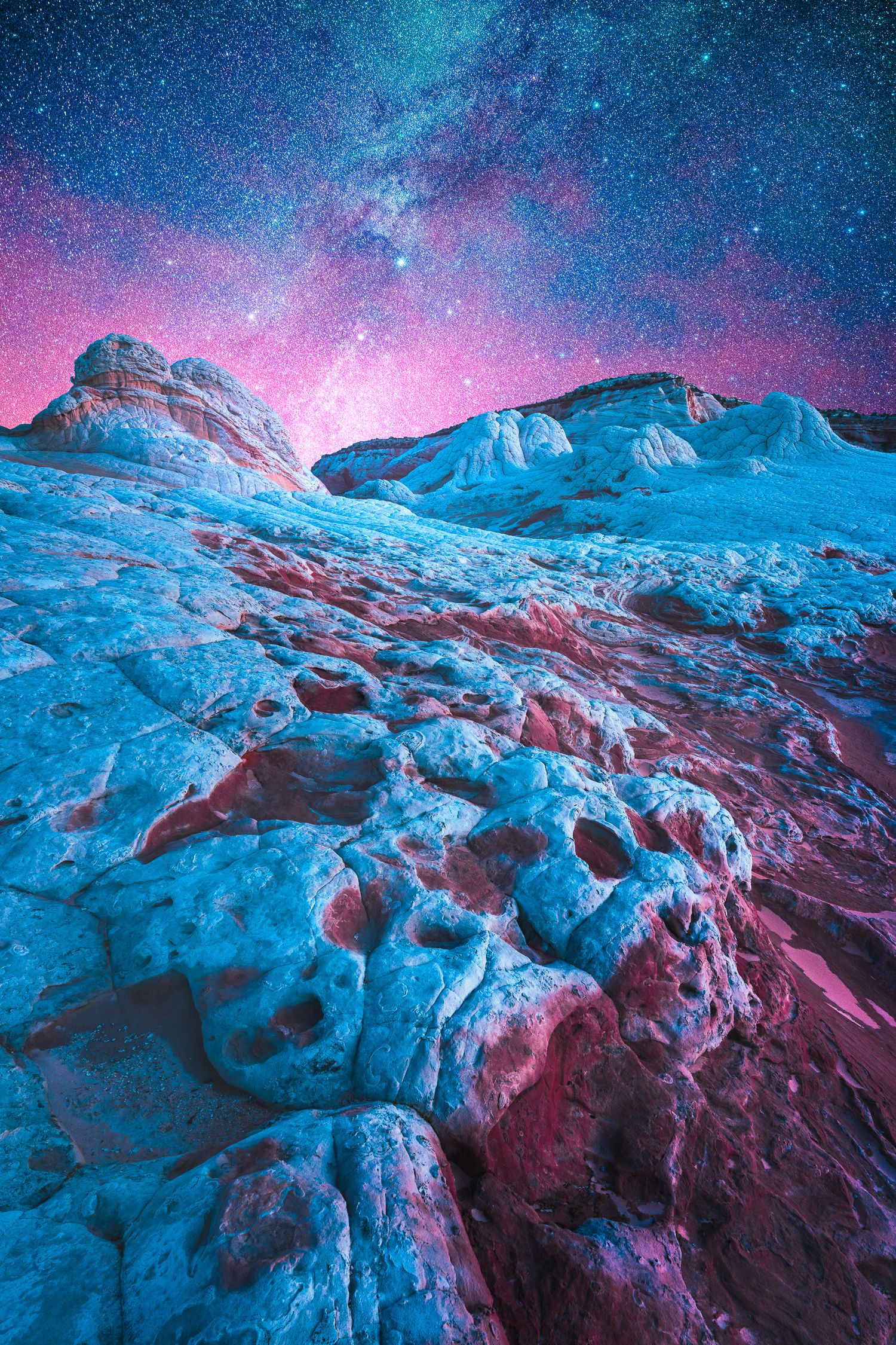White Pocket rock formations glow under a vibrant pink and blue Milky Way night sky in Arizona.