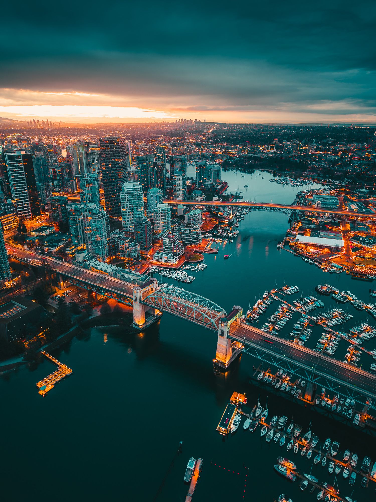 Aerial sunset view of Vancouver city skyline with glowing bridges over False Creek harbor.