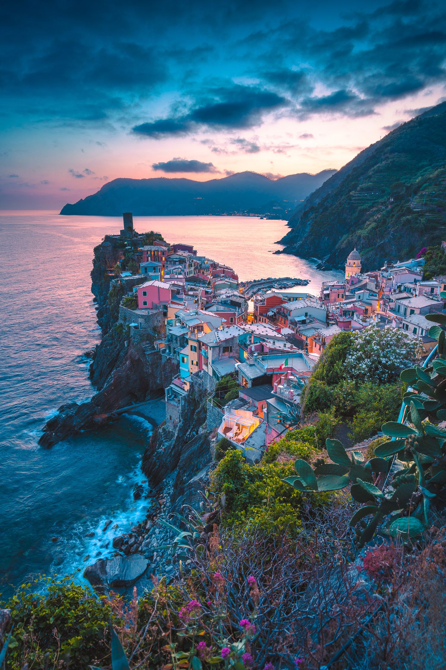 Colorful cliffside village of Vernazza at sunset, Cinque Terre, Italy, with dramatic clouds over the Mediterranean Sea.