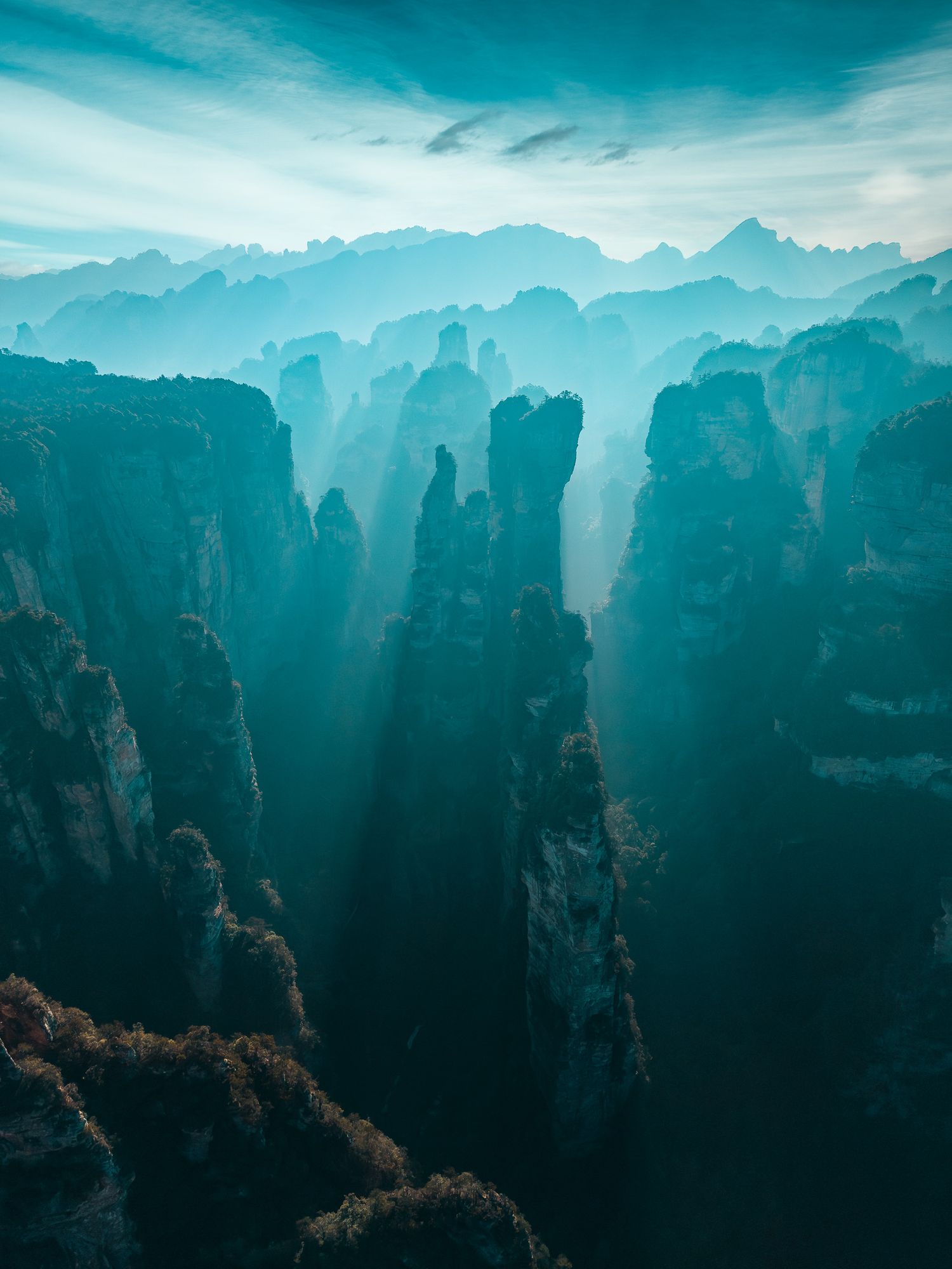 Aerial view of towering karst rock pillars shrouded in blue mist at Zhangjiajie National Forest Park, China.