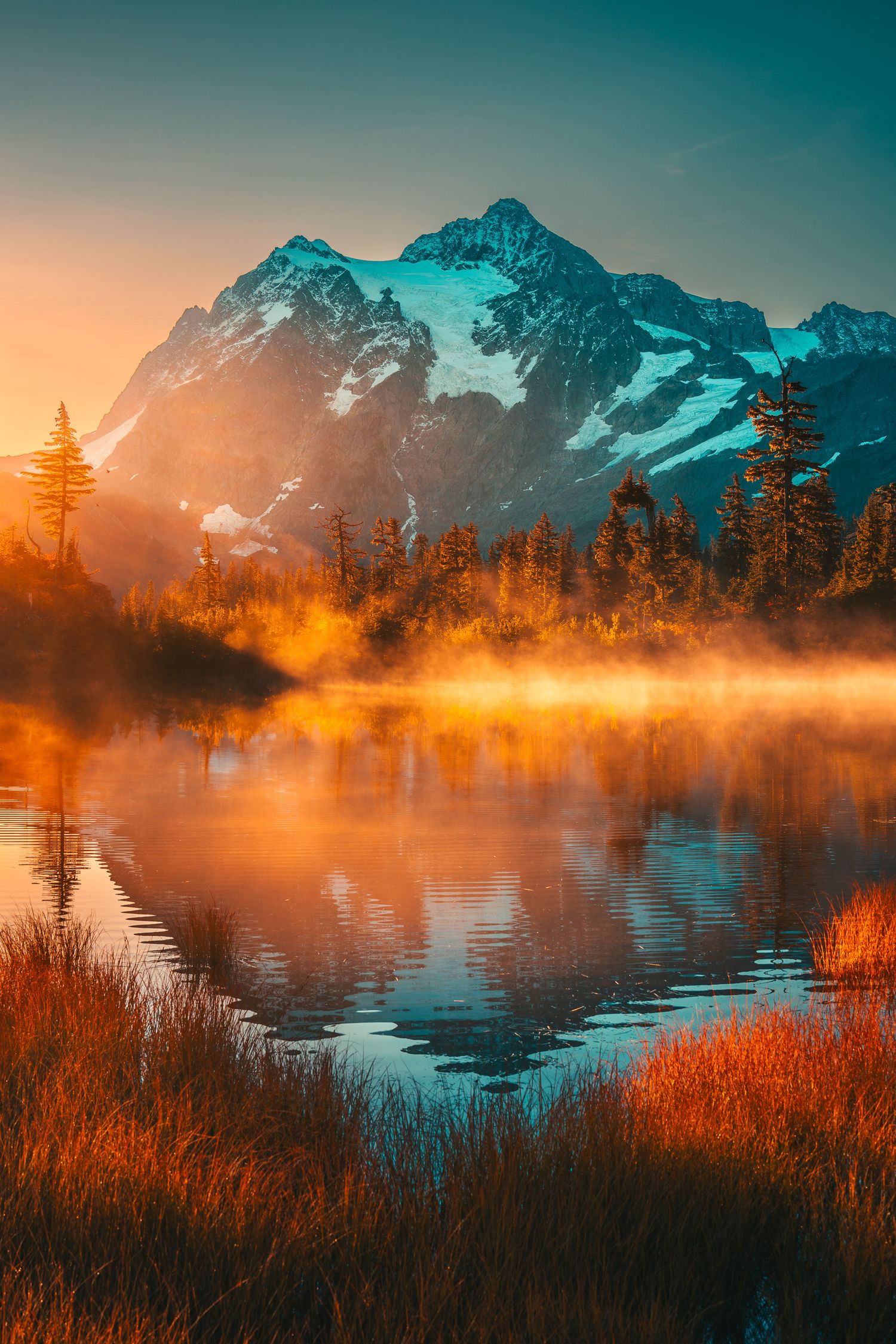 Golden sunrise mist over a serene mountain lake with snow-capped peaks and autumn forest reflections.