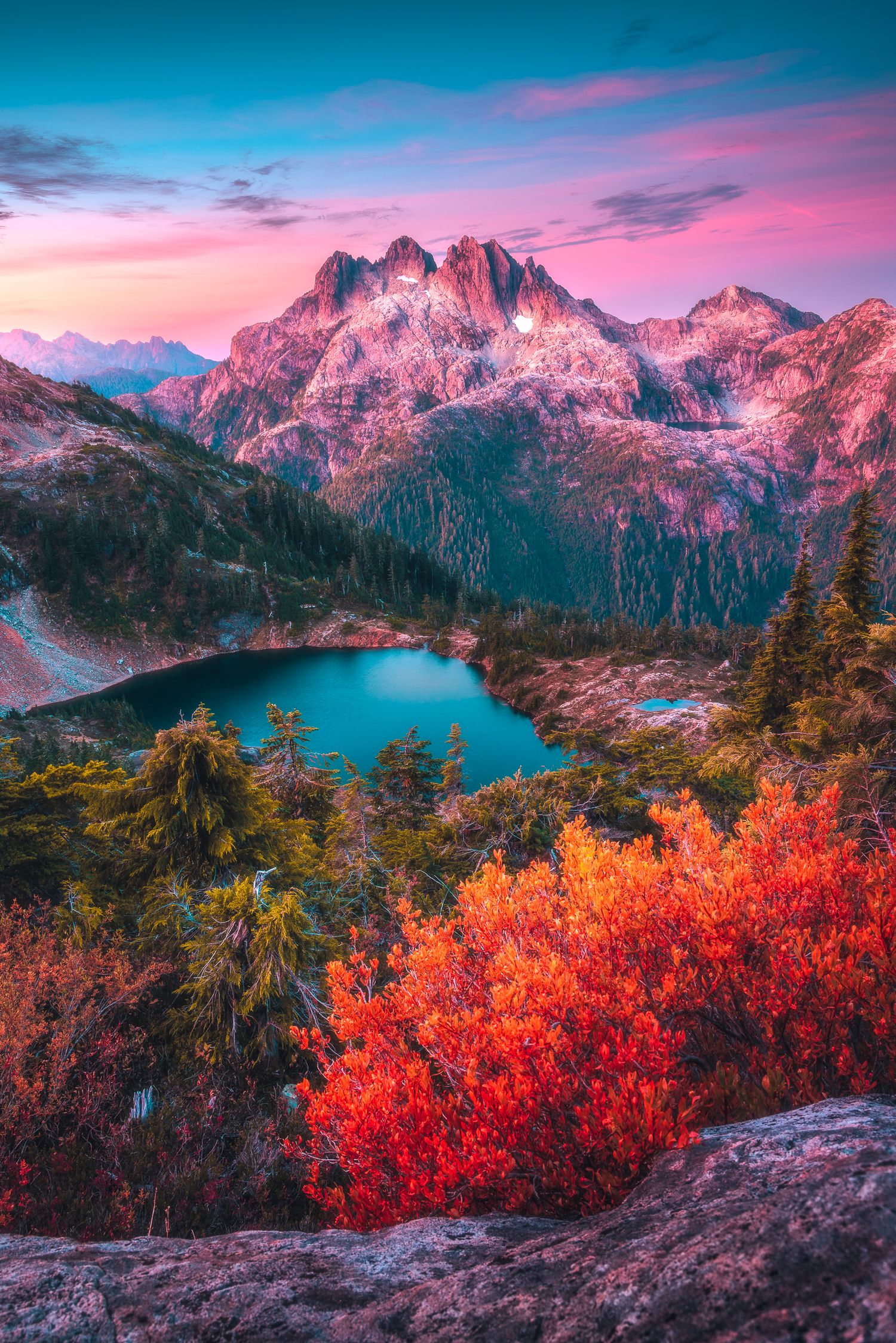 Stunning alpine lake reflecting turquoise waters surrounded by vibrant red autumn foliage and snow-capped mountain peaks at sunset.