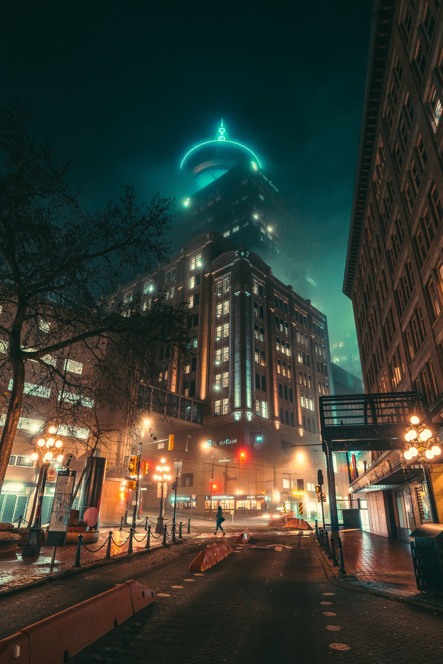 Moody night street view of Vancouver Gastown with glowing heritage building and neon-lit foggy sky.