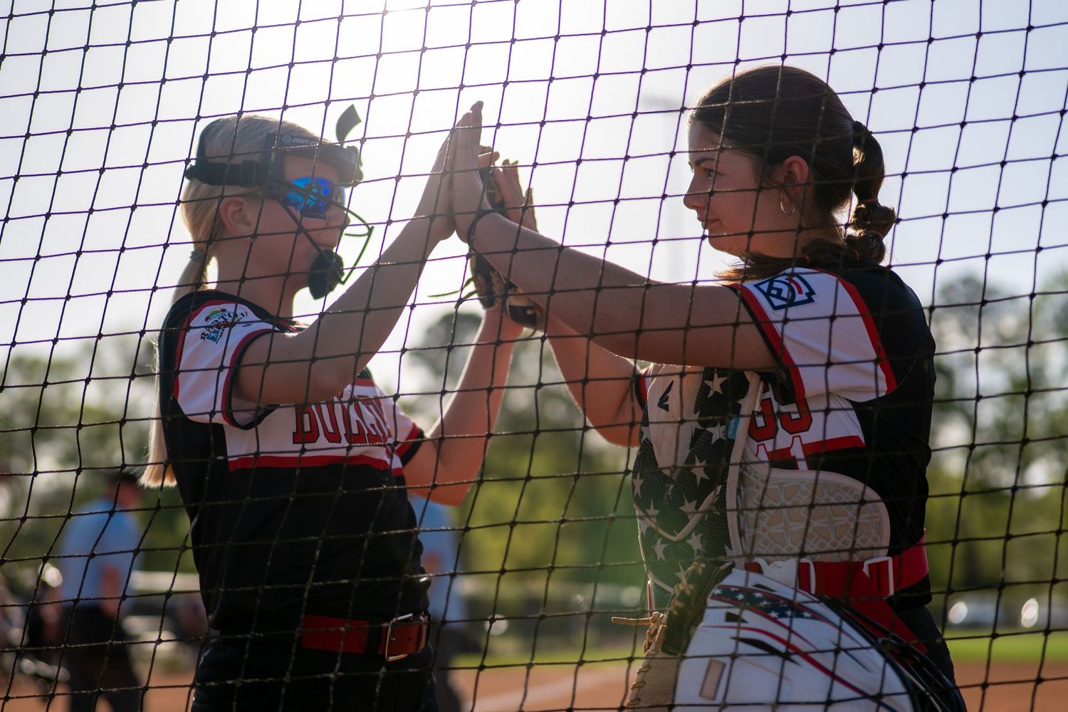 outh softball teammates celebrating with a high five during a game