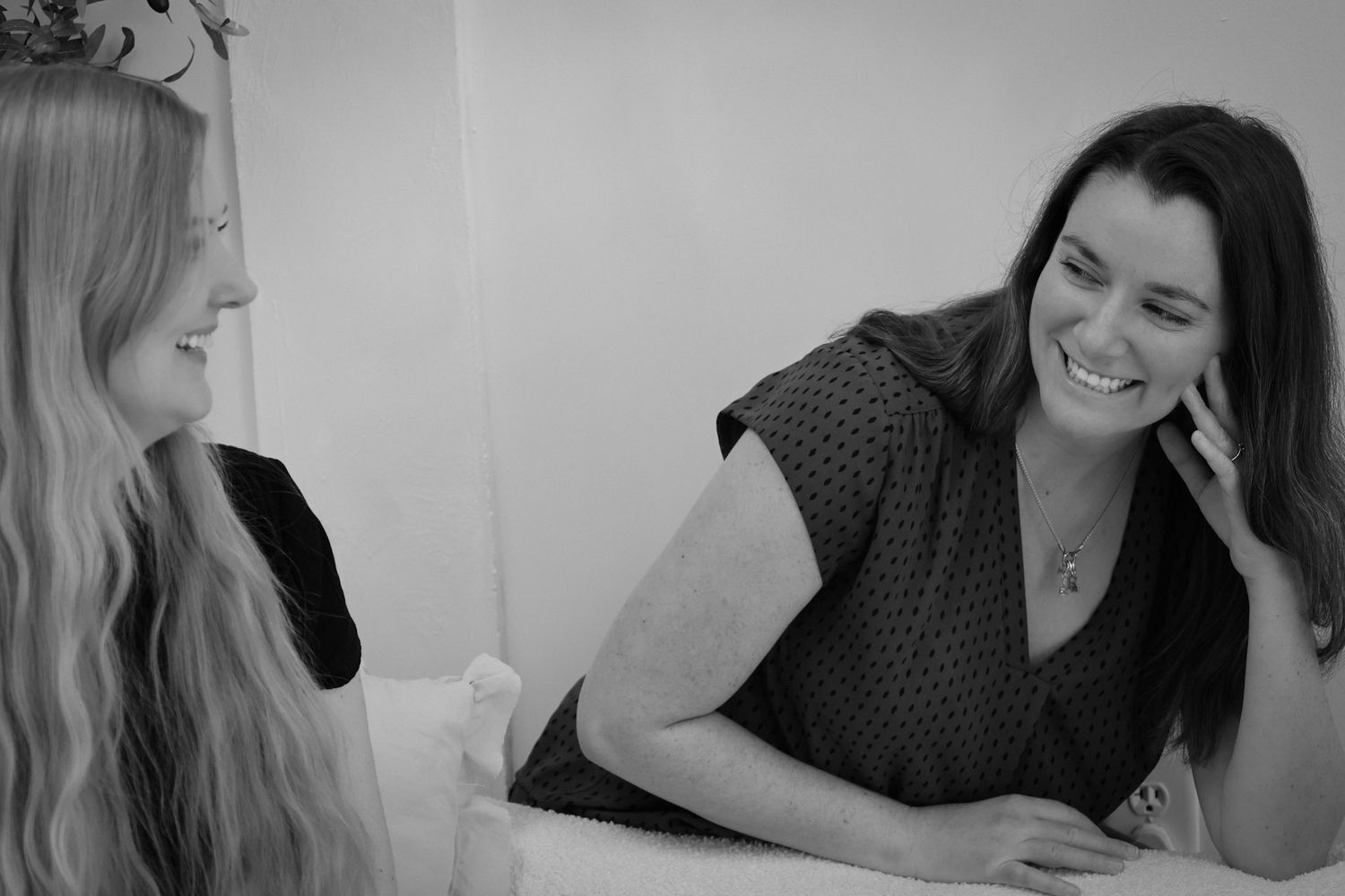 Two women smiling and laughing together in a warm, candid black and white photo.
