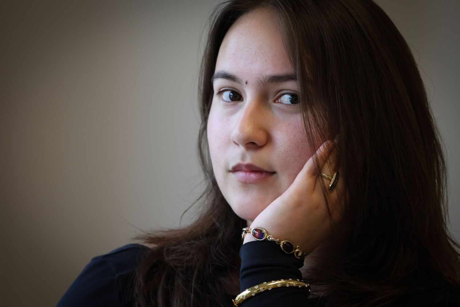 Young woman with dark hair and bindi gazing thoughtfully with hand on her cheek.