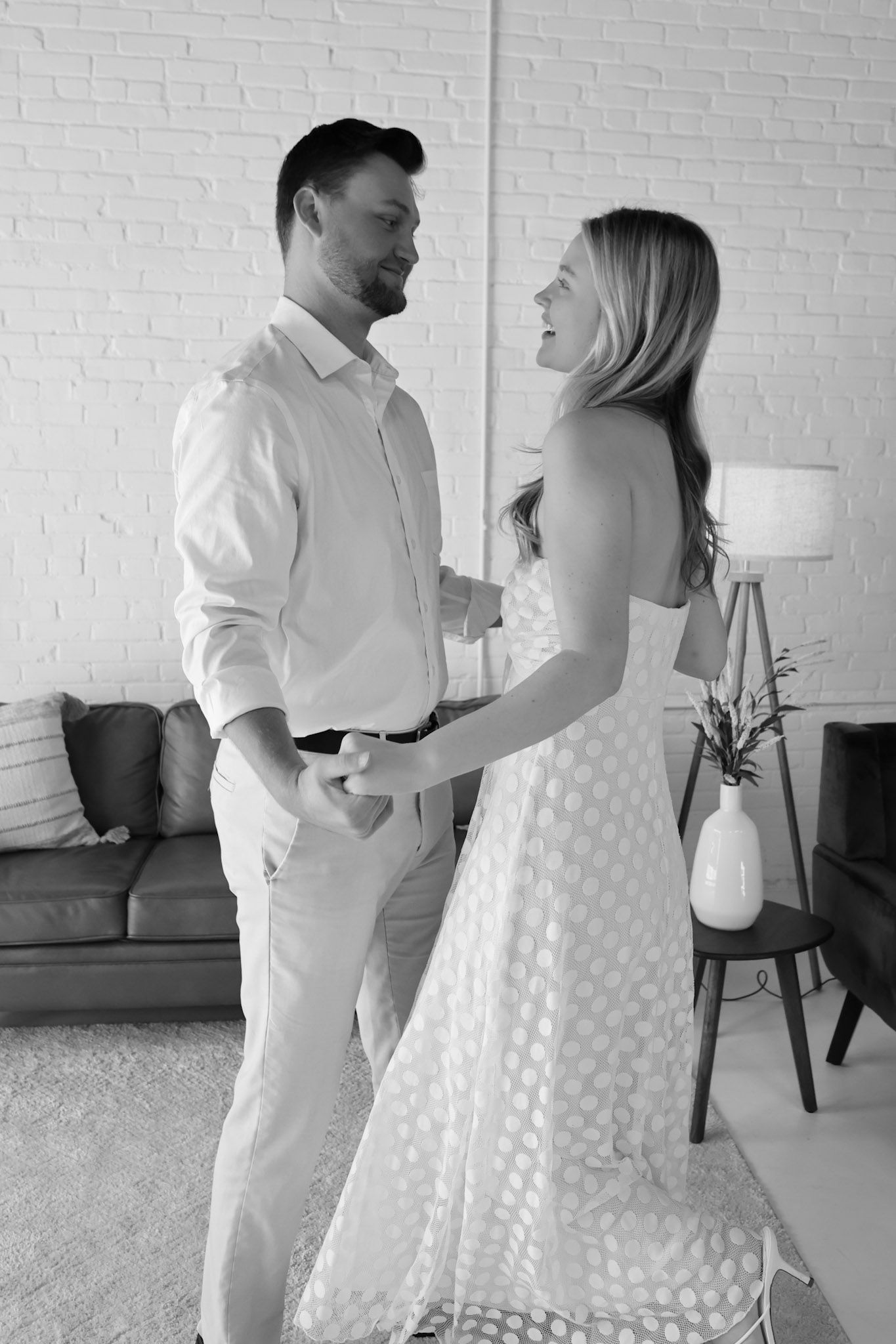 Black and white photo of a couple dancing together in a modern living room, smiling and holding hands.