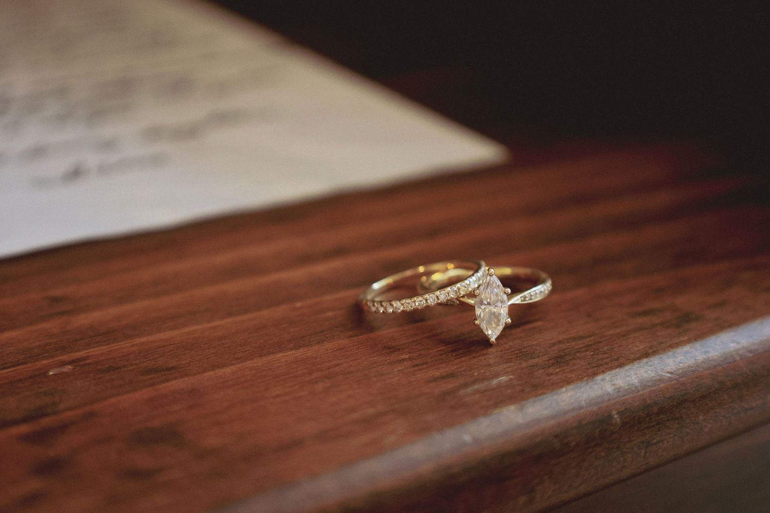 Gold diamond engagement ring with marquise-cut center stone resting on a wooden surface beside a handwritten love letter.
