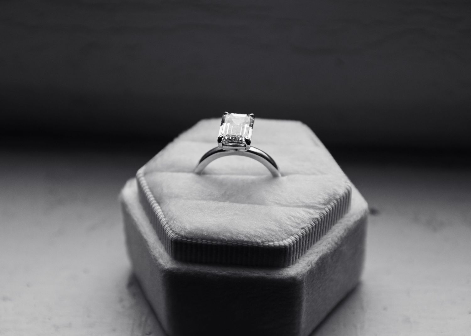 Black and white photo of a solitaire diamond engagement ring displayed in a hexagonal velvet ring box.