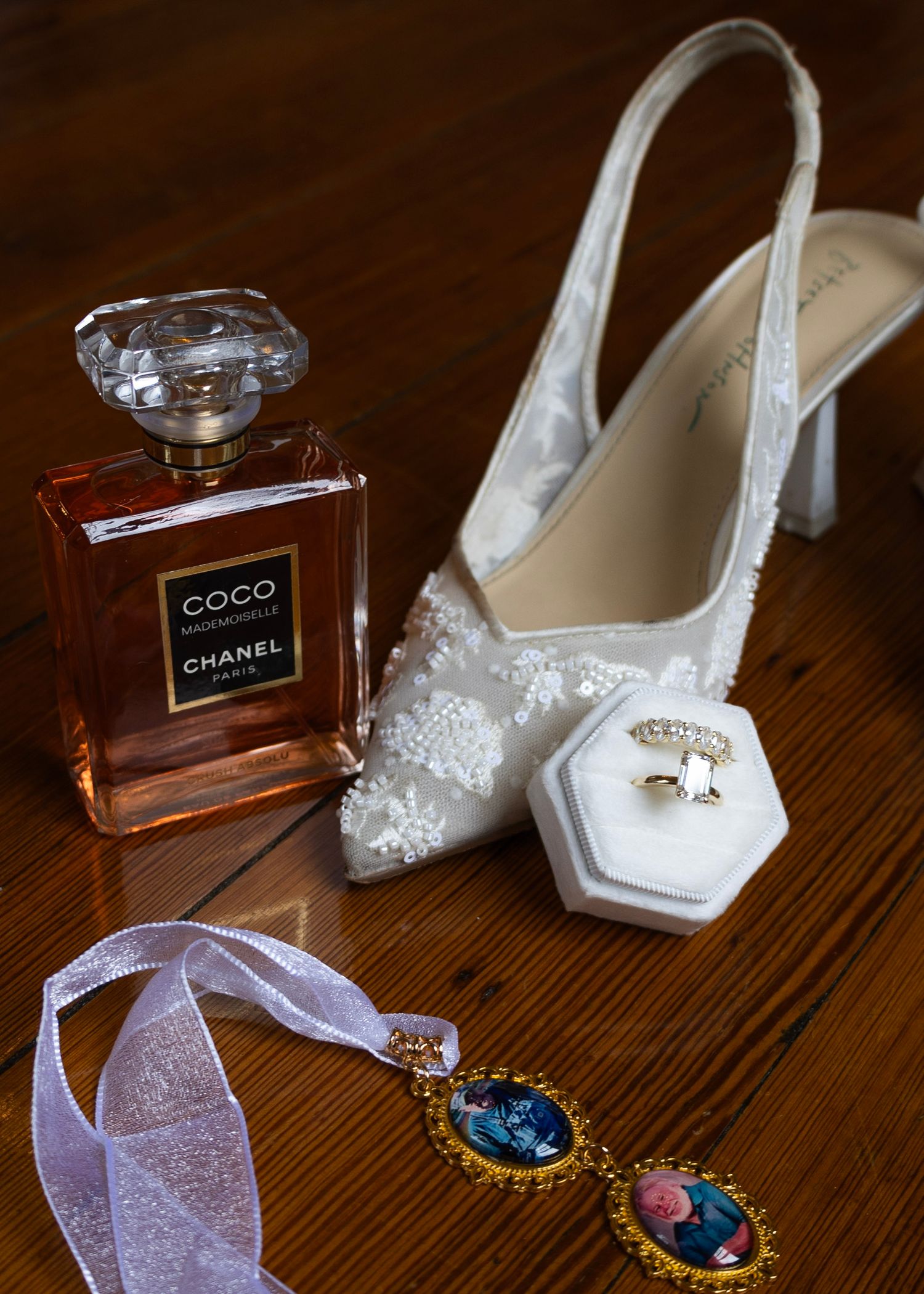Bridal flat lay featuring Chanel Coco Mademoiselle perfume, white lace heels, diamond ring, and gold photo charm bouquet pins.