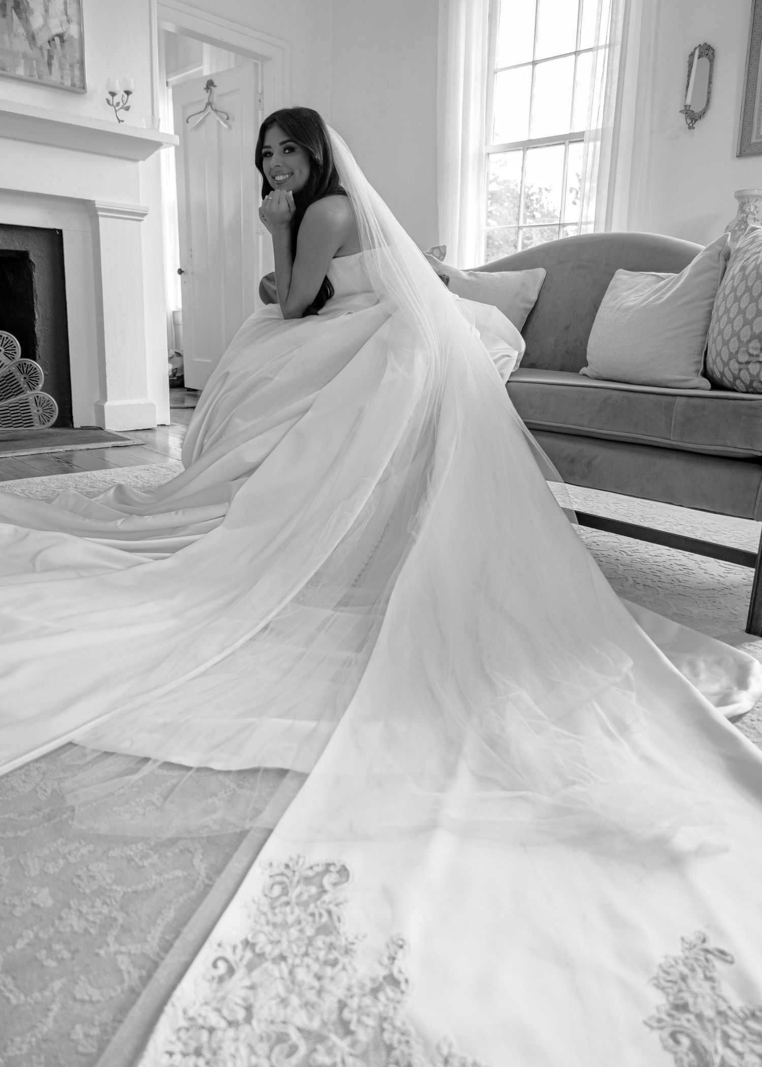 Bride in a stunning white wedding gown with long cathedral veil in an elegant room, black and white photo.