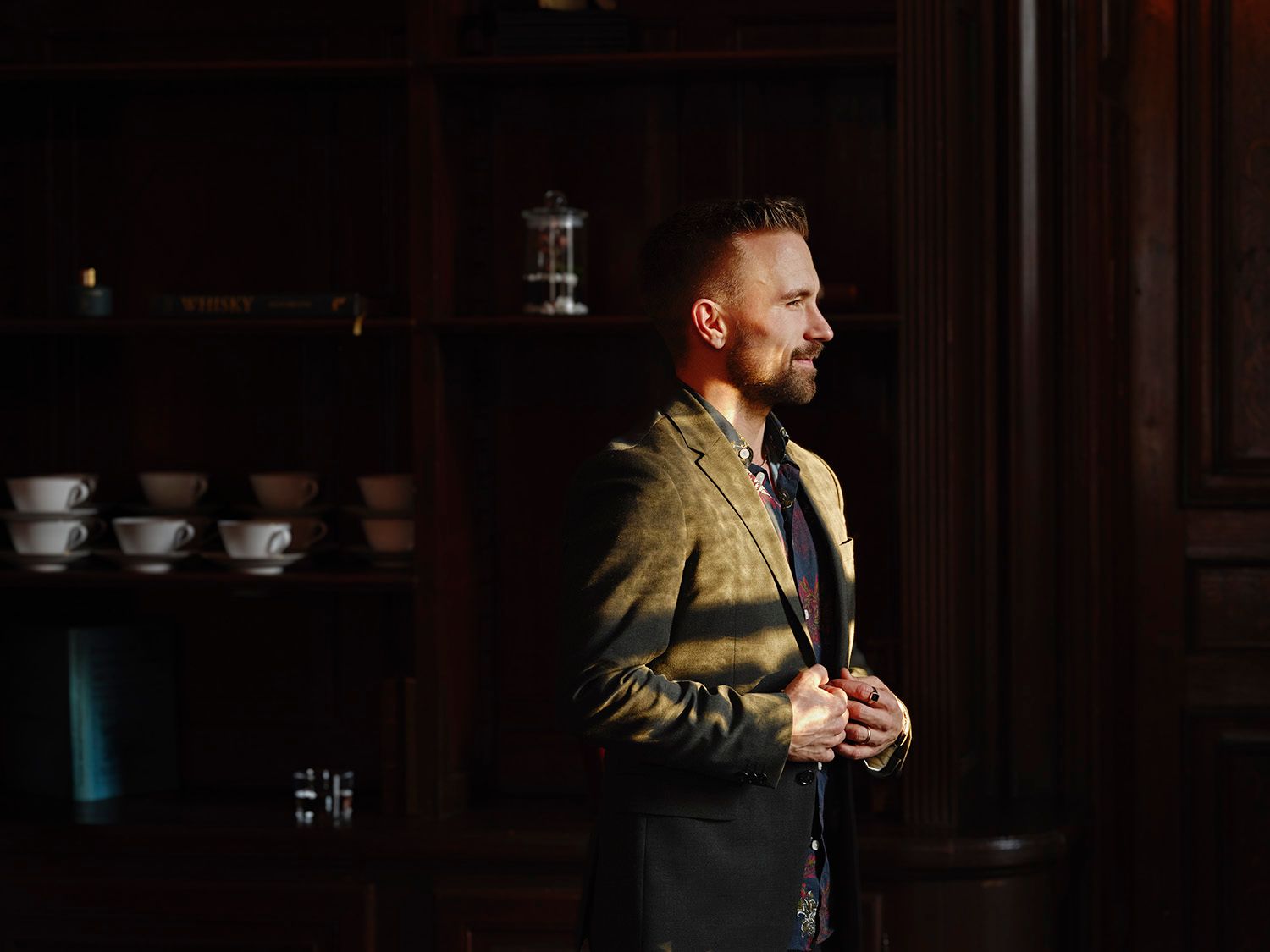 Man in gold blazer standing in dramatic side lighting indoors.