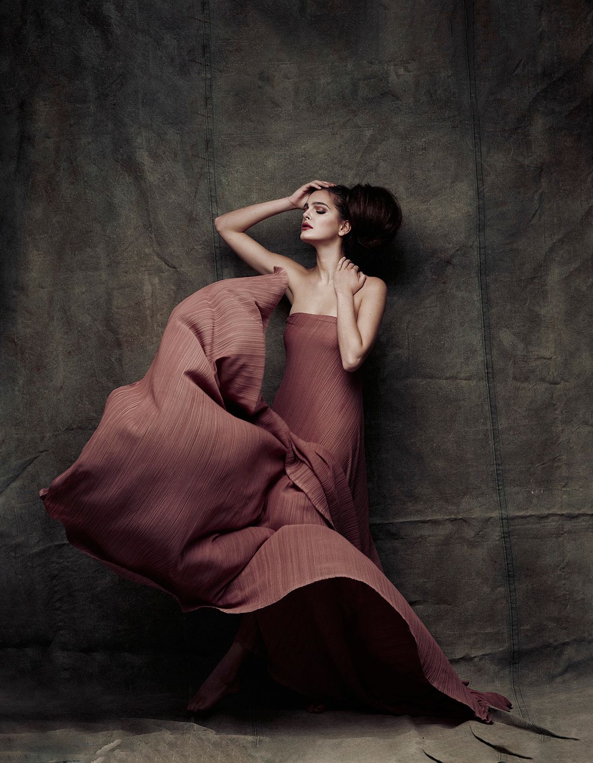 Woman in flowing pink gown posed dramatically against textured backdrop.