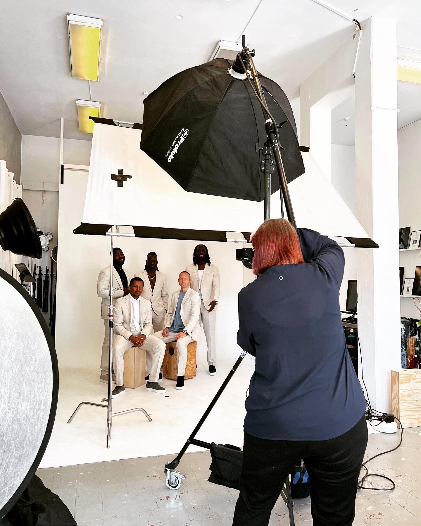 Photographer with red hair shooting a group portrait in a professional studio with softbox lighting.