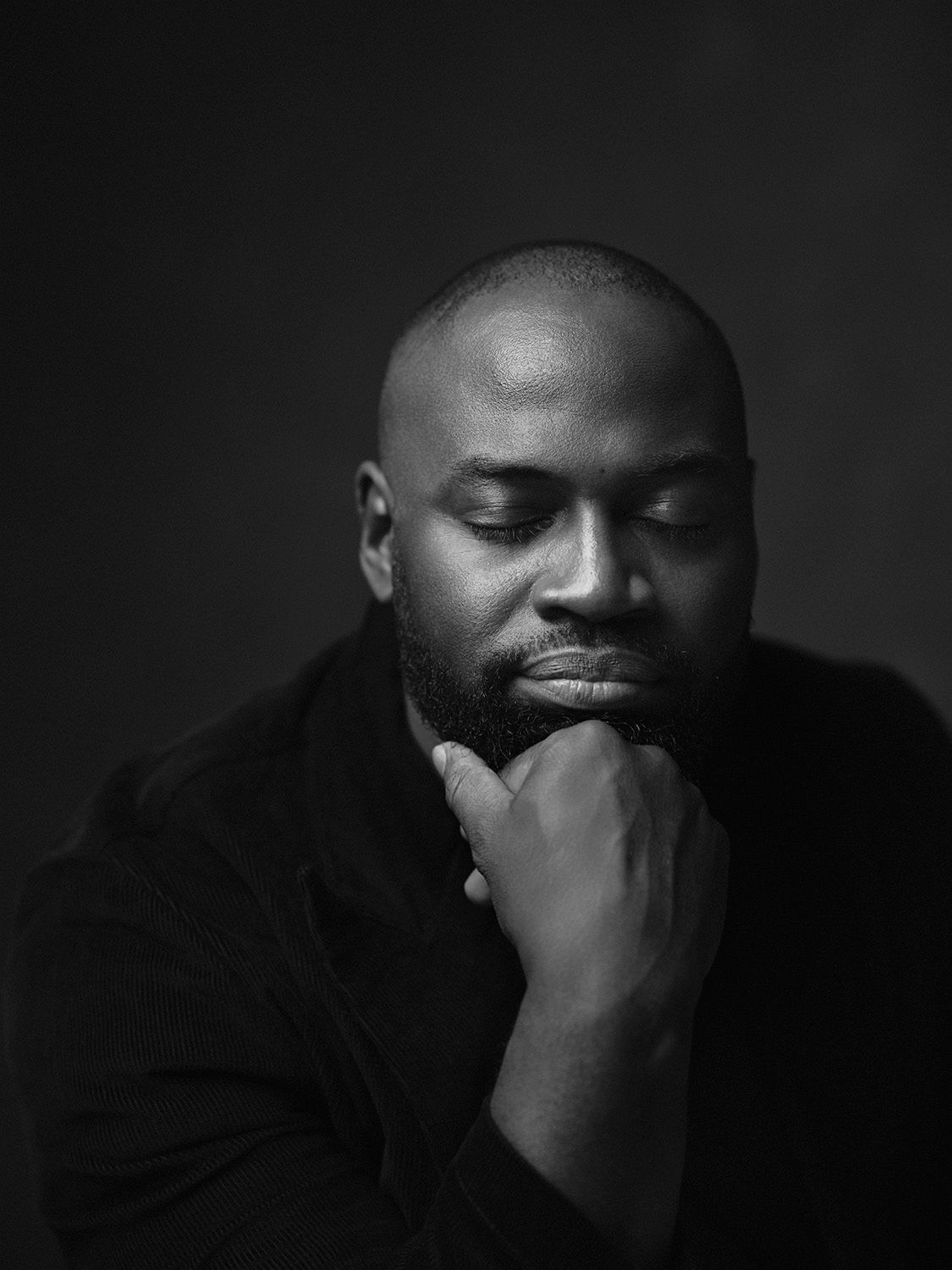 Black and white portrait of a man with a beard resting his chin on his hand.