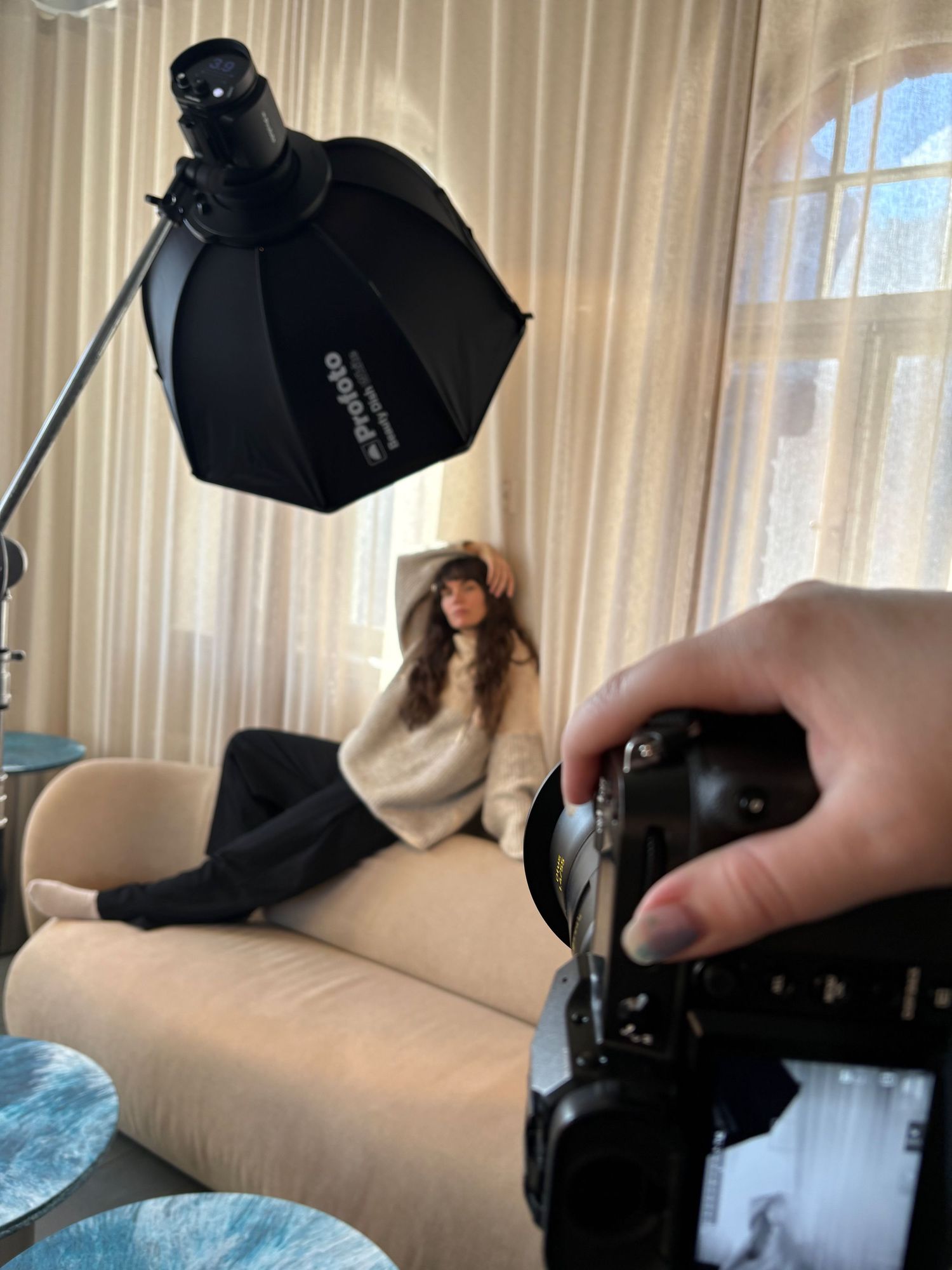 Behind-the-scenes photo shoot with a woman on a cream sofa lit by a Profoto octabox softbox light.