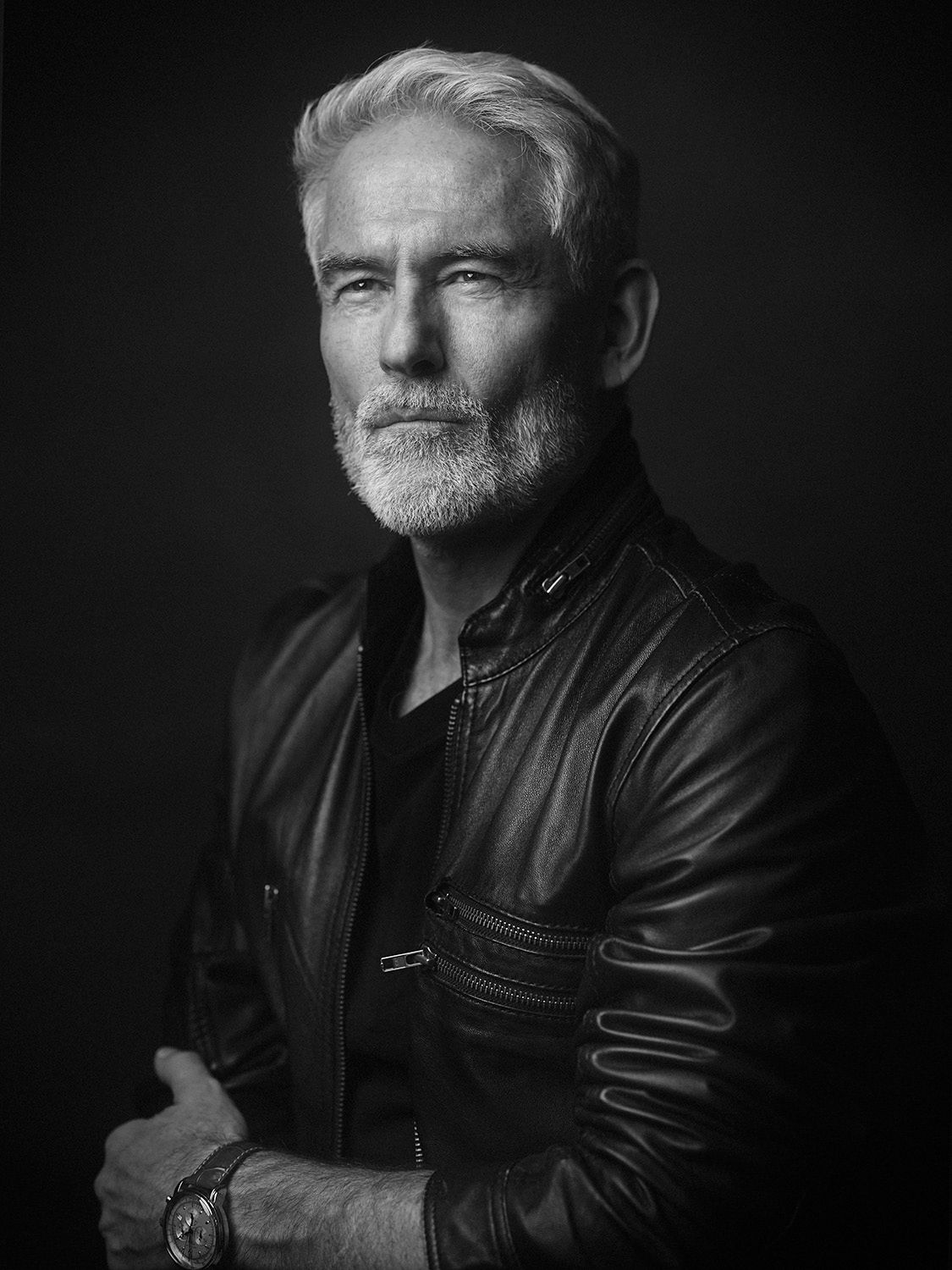 Black and white portrait of a distinguished older man with silver hair and beard in a leather jacket.