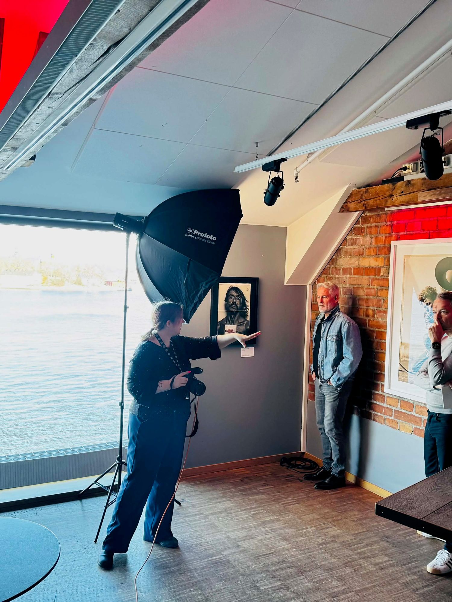 Professional photographer using a softbox light to photograph a man against a wall in a modern studio.