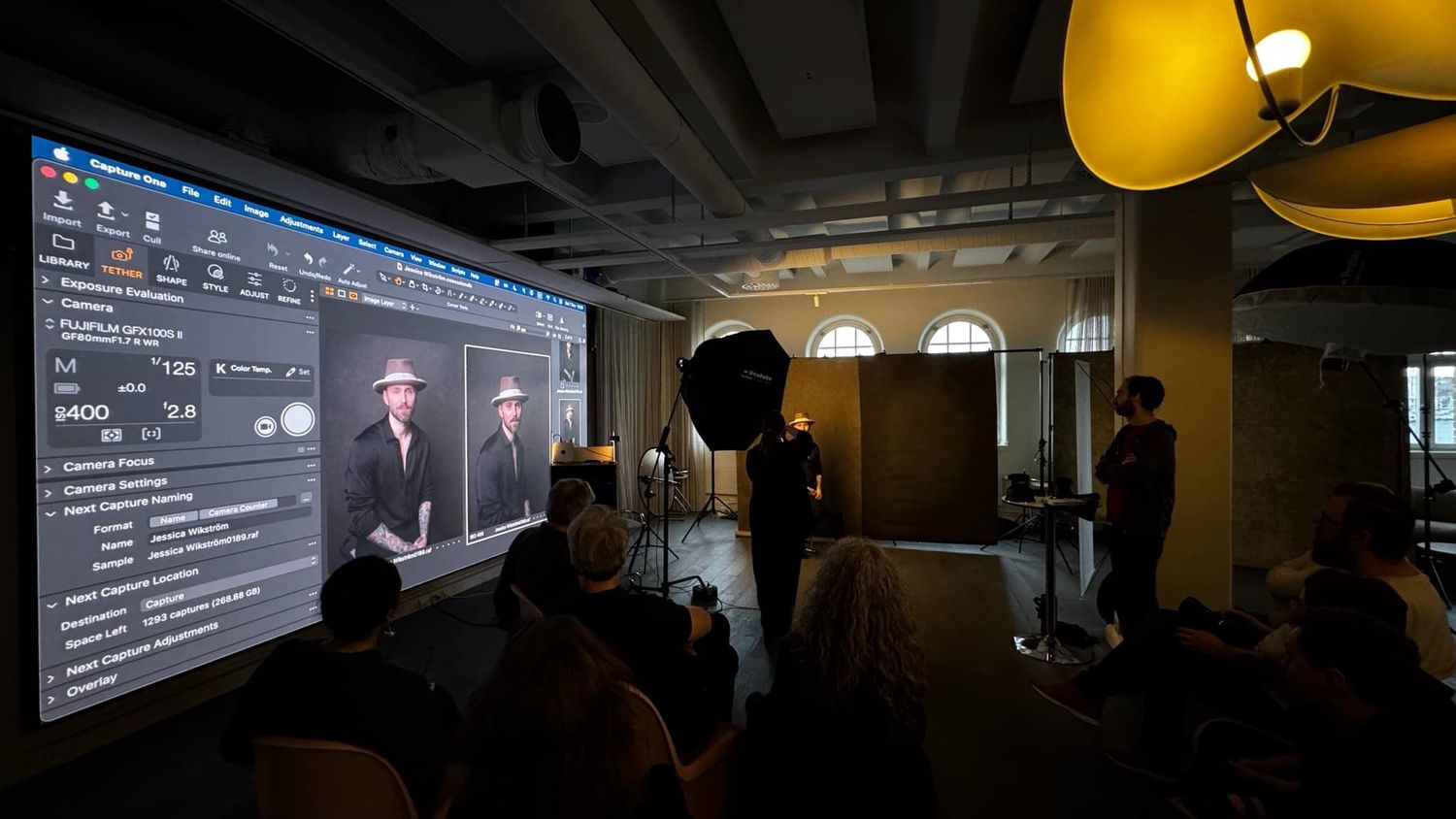 Photography workshop with audience viewing a projected portrait editing session on a large screen.