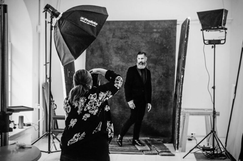 Behind-the-scenes photo shoot in a studio with professional lighting equipment and a photographer capturing a male subject.